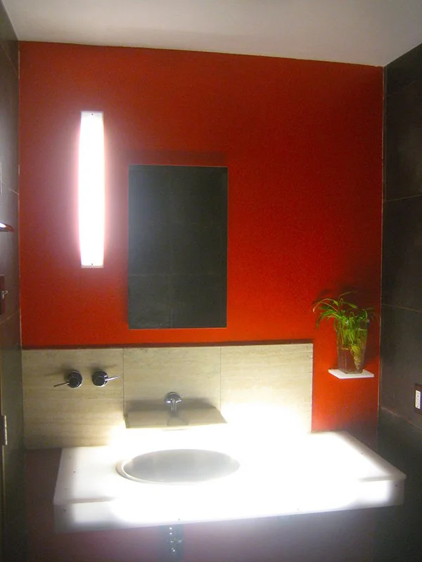 Modern powder room with a glowing illuminated vanity, vibrant red accent wall, and sculptural lighting.