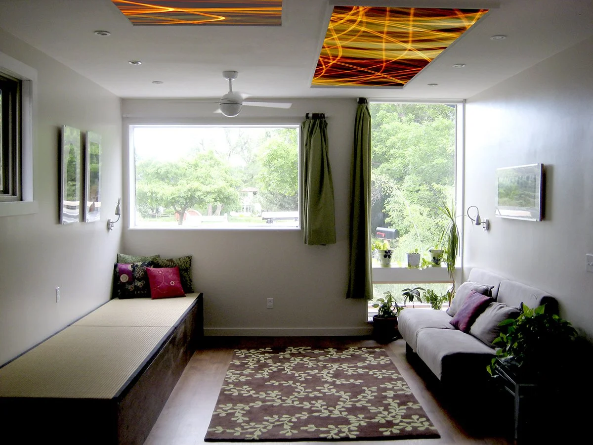 Modern living room with interchangeable illuminated ceiling panels, built-in bench seating, and expansive windows bringing daylight into the space.