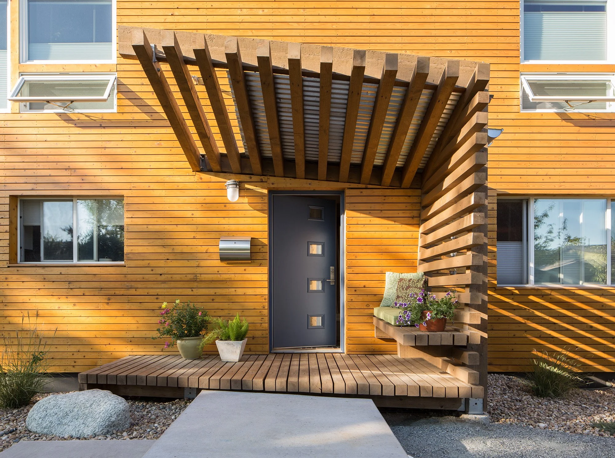Front entry of the Erosion House featuring a sculptural cedar porch carved from layered horizontal slats inspired by natural erosion.