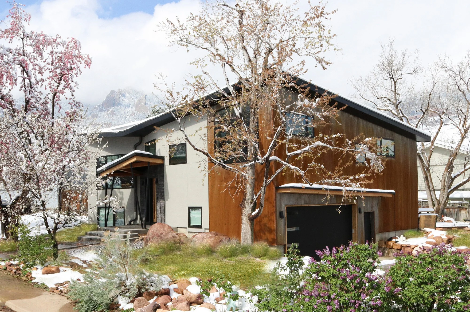 Modern custom home in Colorado designed by AsOne Architecture featuring folded roof forms, vertical cedar siding, white stucco, and a contemporary entry integrated into a mature landscape.
