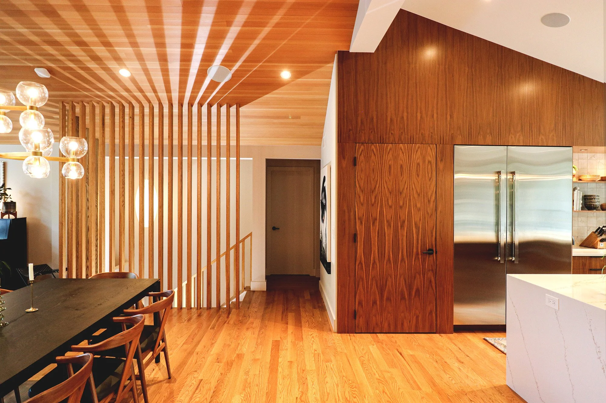 Custom walnut millwork, sculptural slatted screens, and a continuous wood ceiling organize this modern Boulder residence into a flowing sequence of living, dining, and kitchen spaces inspired by the experience of moving through a canyon.