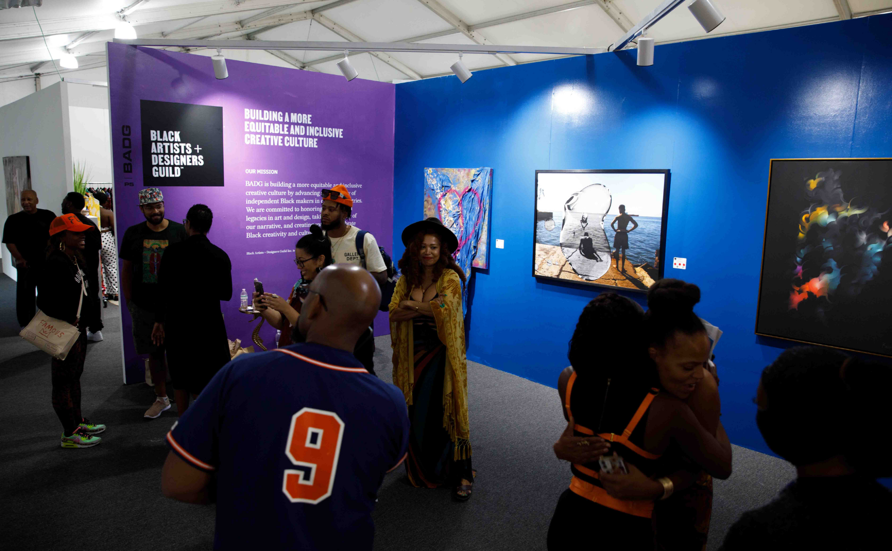 People viewing artwork and engaging at Black Artists + Designers Guild exhibition in an art gallery with purple and blue walls.