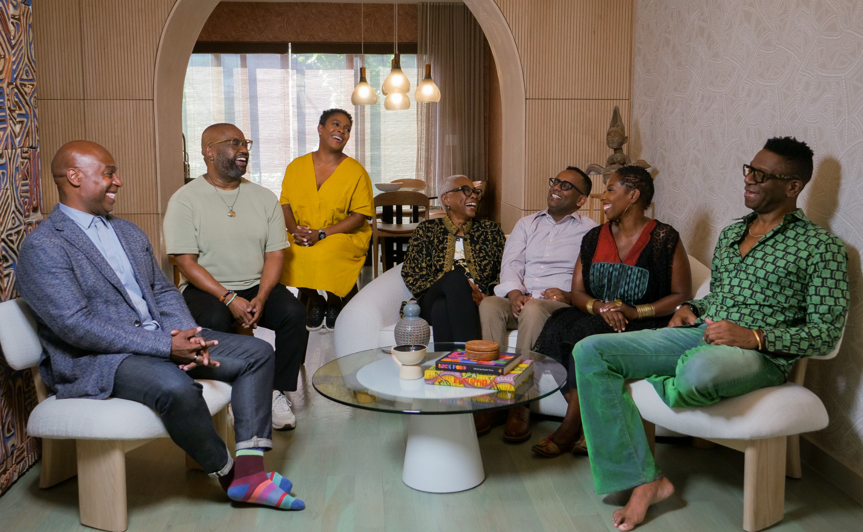 BADG, A group of seven diverse adults enjoying a lively discussion in a cozy, stylish living room.