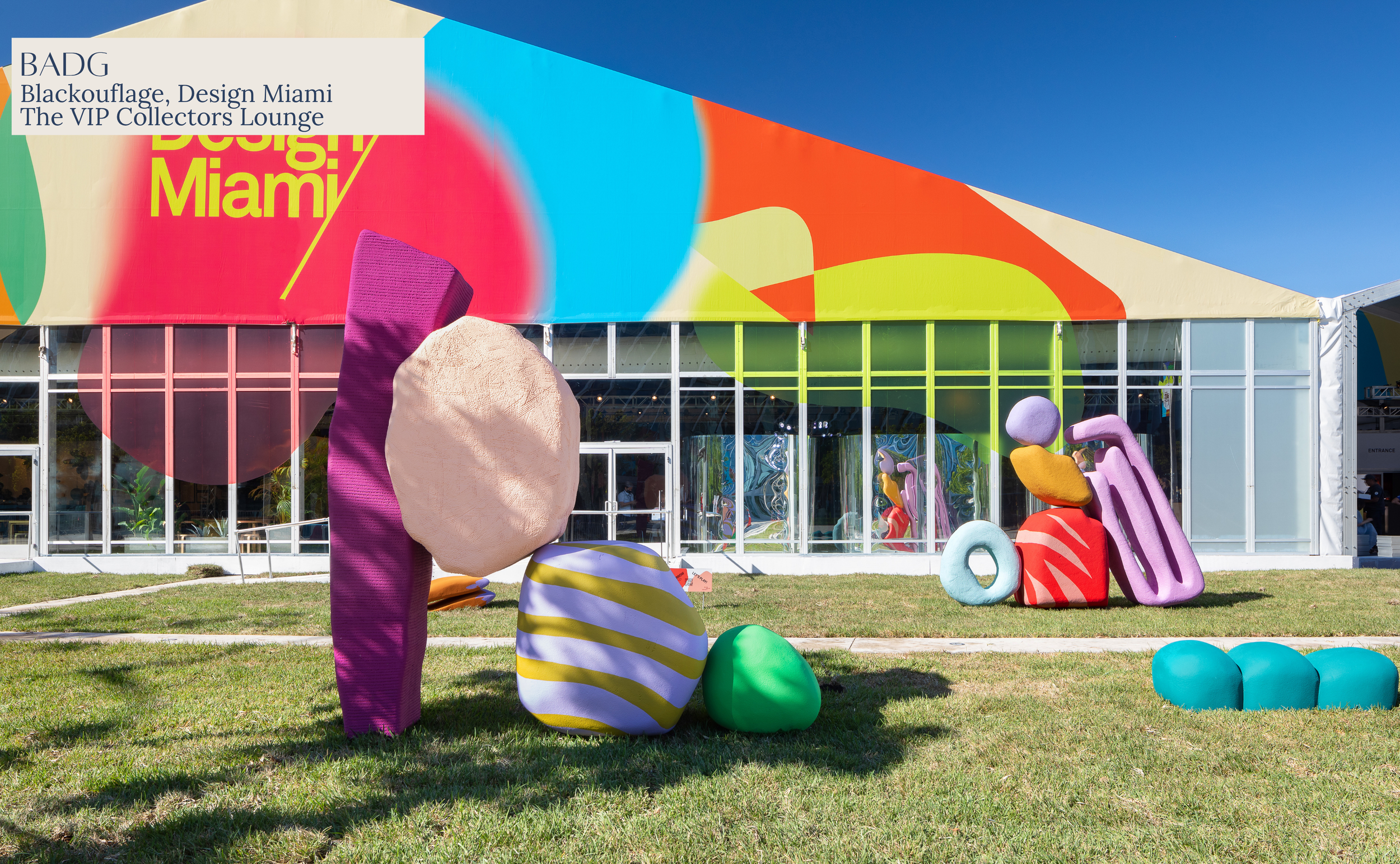 Colorful outdoor art installation with organic shapes and textured surfaces in front of a building with a vibrant, abstract mural.