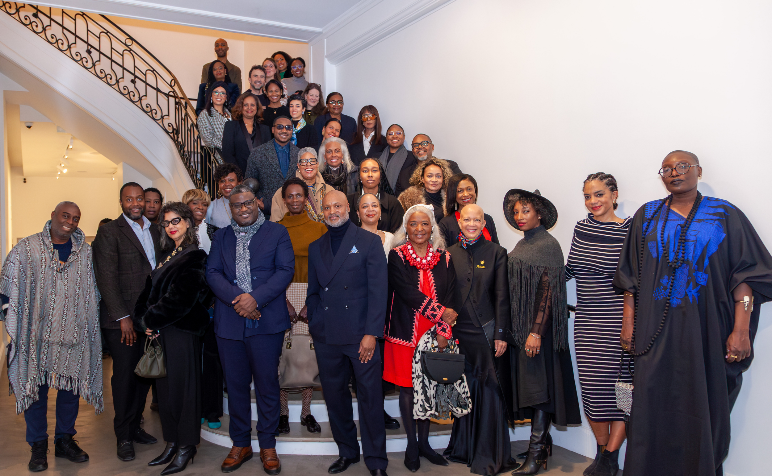 Group of diverse people gathered on a staircase, posing for a photo at an indoor event, dressed in formal and stylish attire.