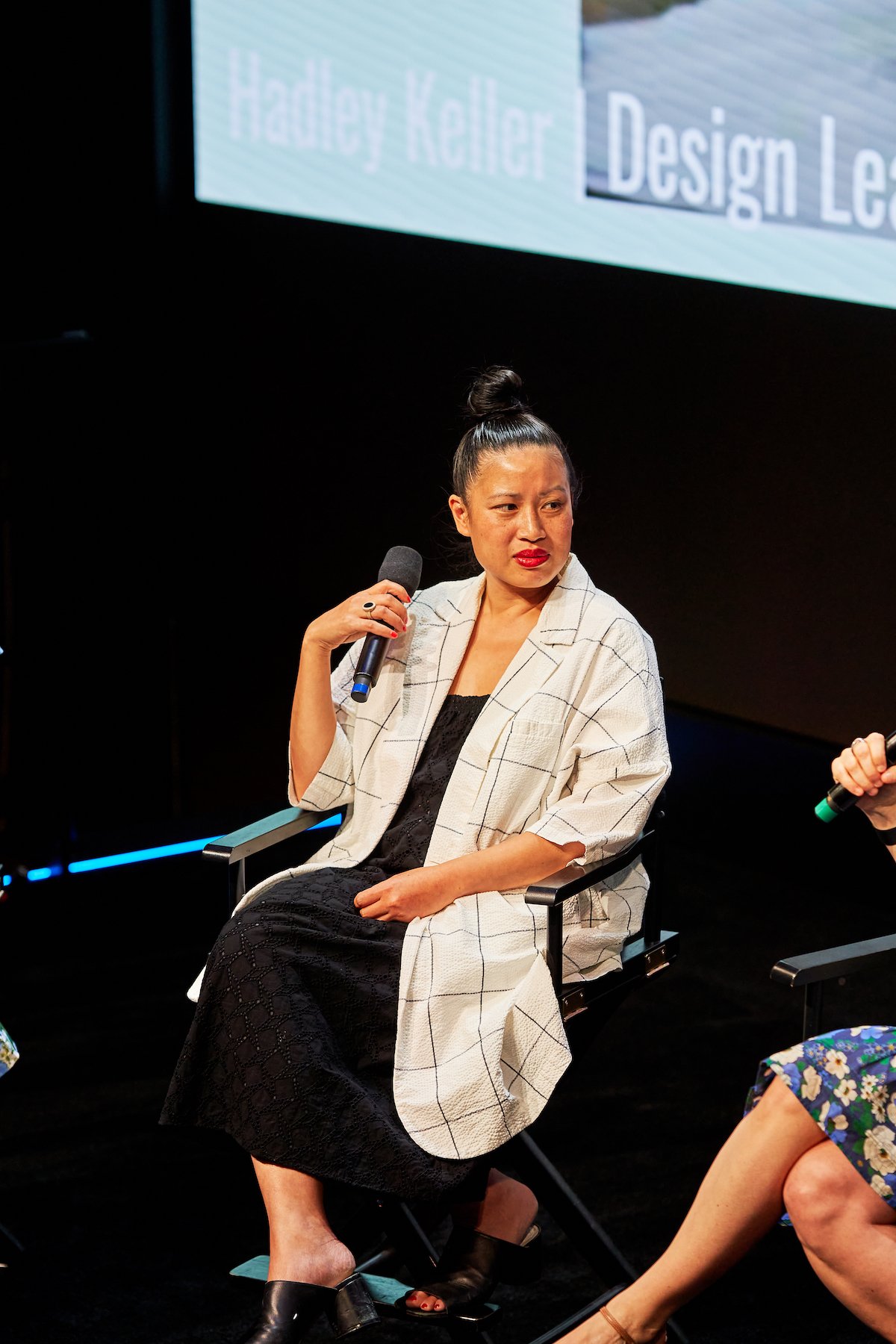 A woman sitting on a chair, holding a microphone, participating in a discussion or panel at an event.