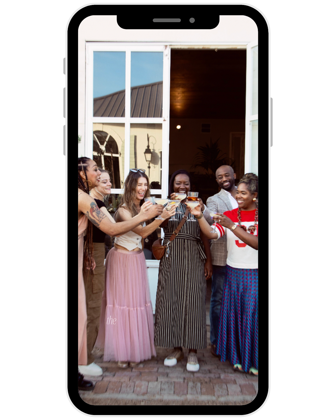 A group of diverse friends celebrating with drinks outside a house, smiling and toasting.