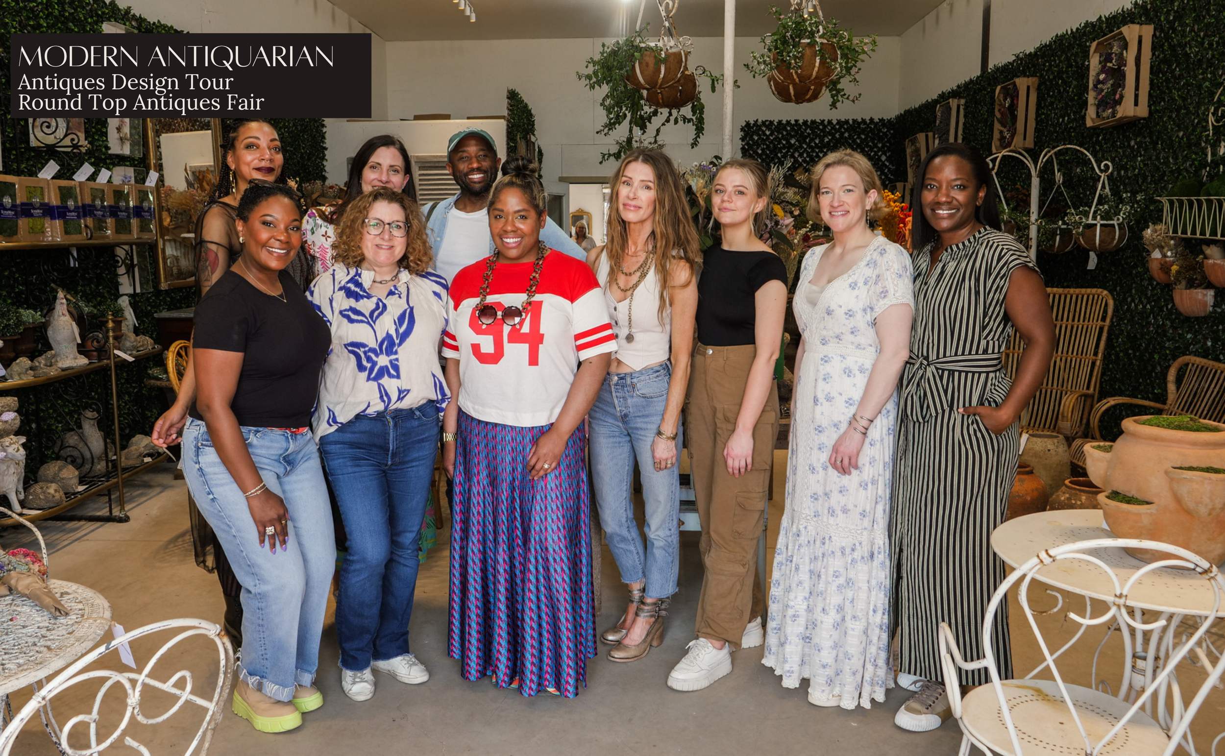 Group of people posing in an antique store during a modern antiquarian antiques design tour event, surrounded by vintage and decorative items.