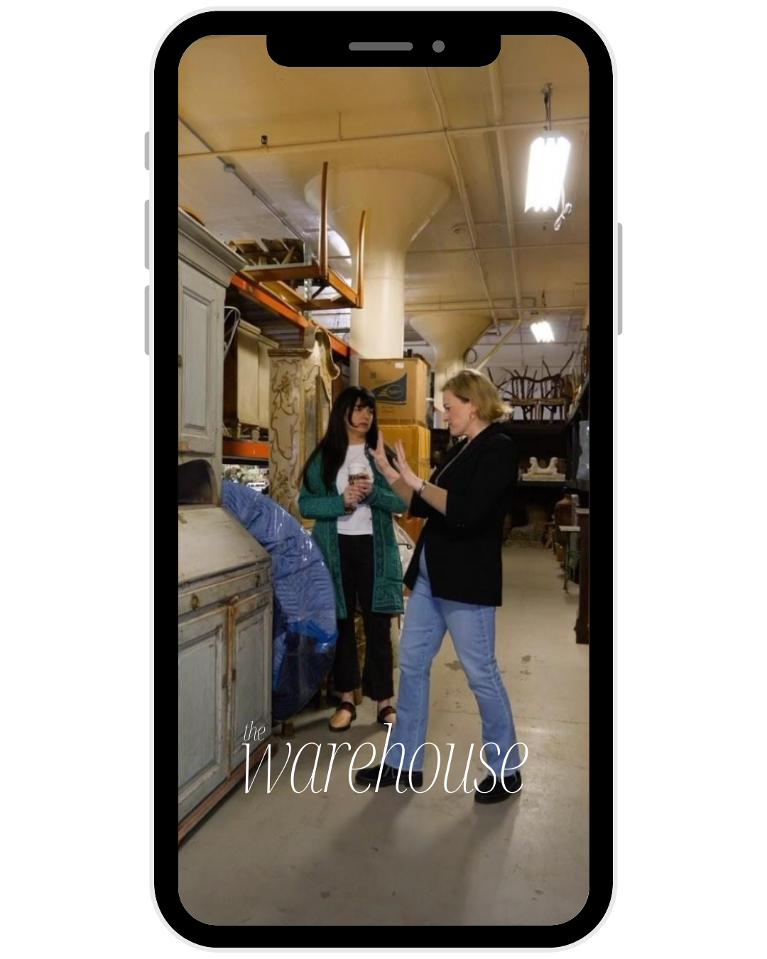 Two women having a conversation in a warehouse with shelves and boxes.