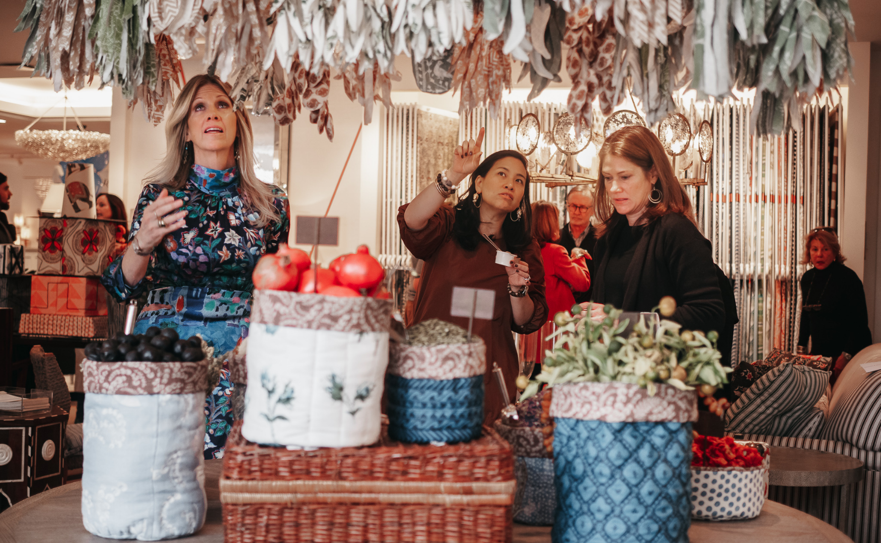 Women shopping for holiday decorations with baskets of artificial fruits and plants on a table
