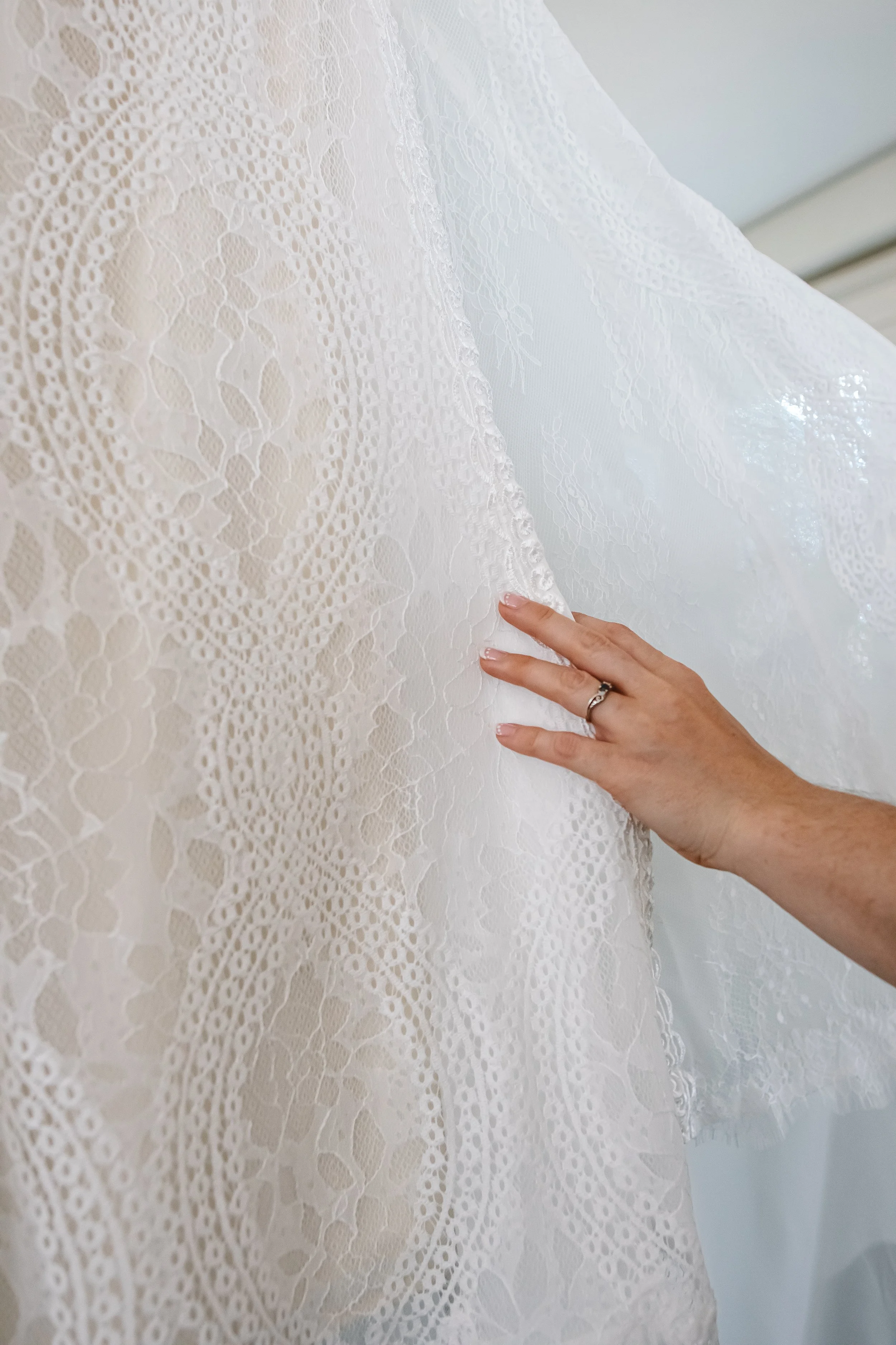 Close-up of a hand touching a white lace fabric, possibly a wedding dress, with intricate lace patterns.