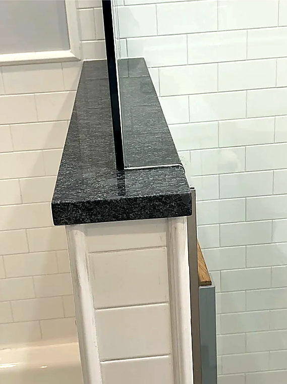 half wall separating the bathtub from the shower, glass panel set on granite wall cap