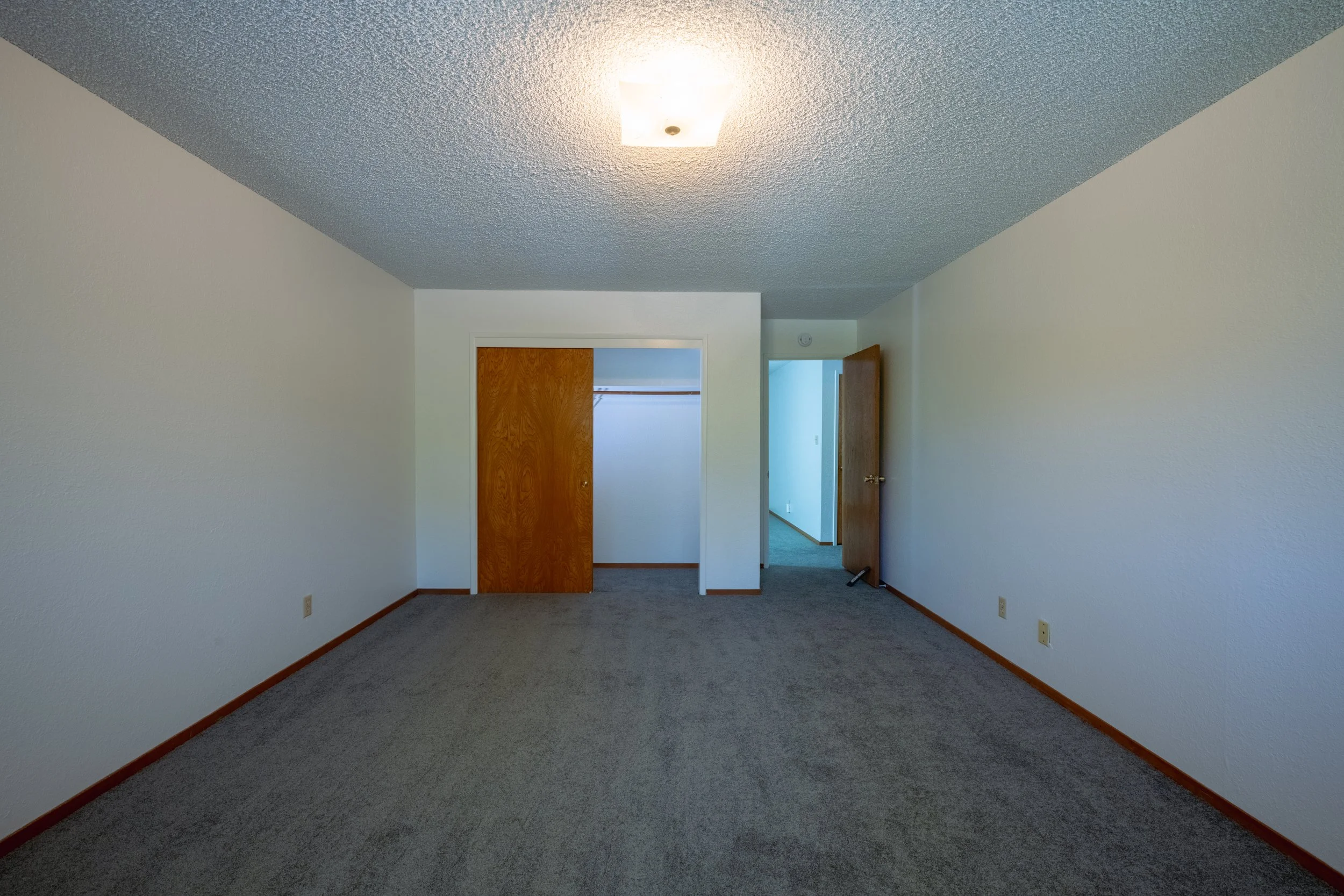 Apt. F Canary Apartments in Calistoga, CA. Empty room with beige carpet, white walls, closet with wooden doors, and an open door leading to a hallway.