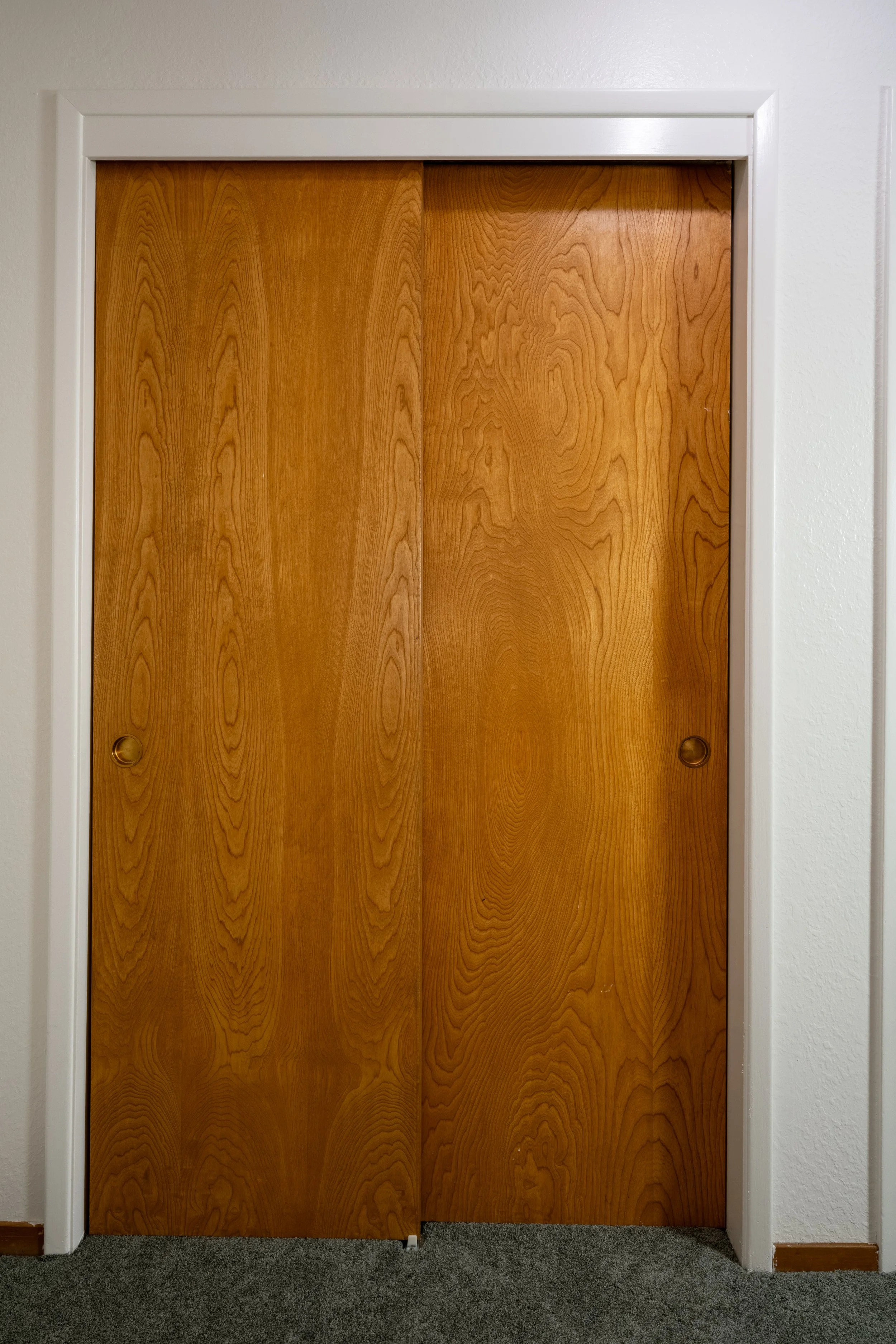 Wooden sliding closet doors in a room with white walls and gray carpet.