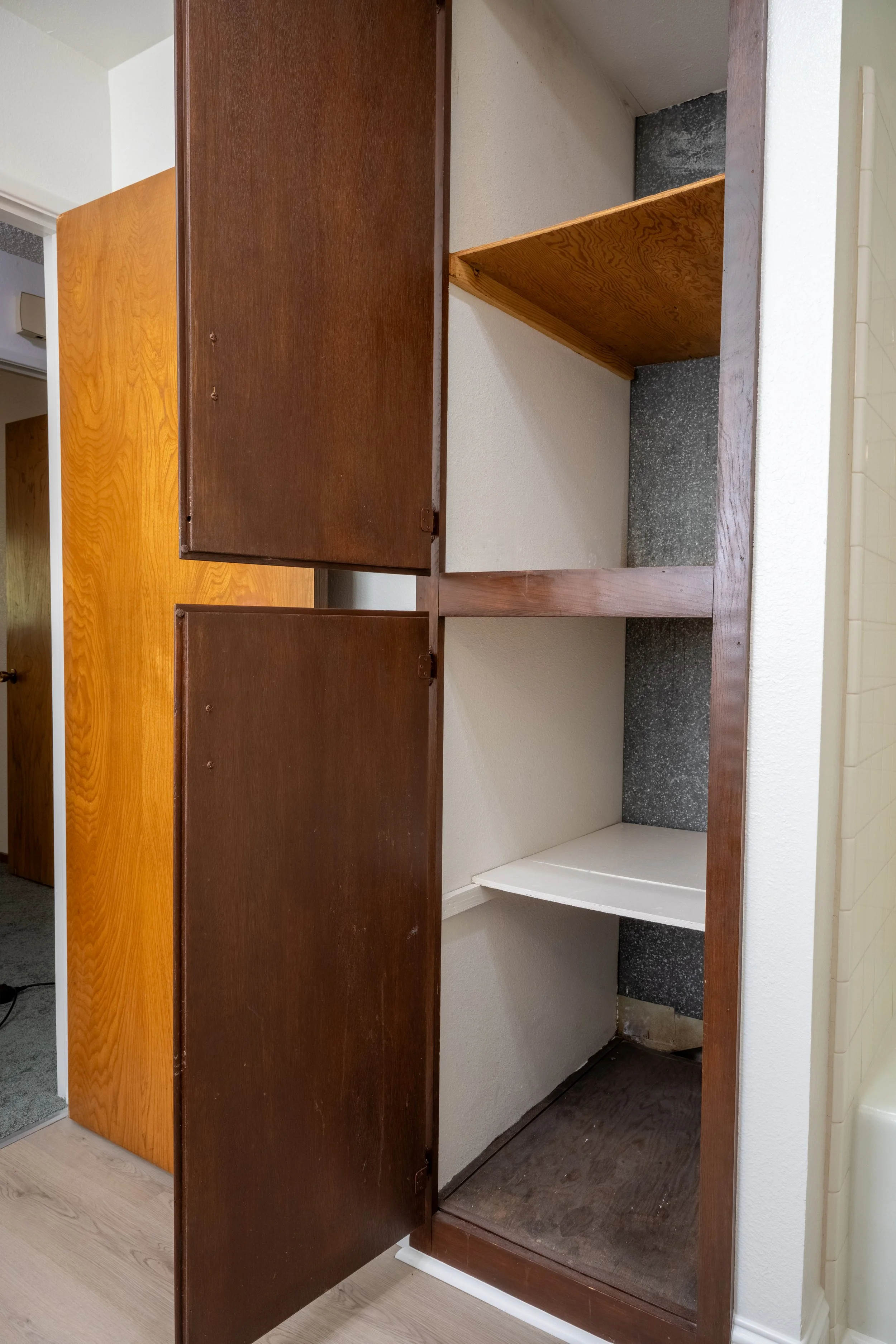 Apt. F: Canary Apartments in Calistoga, CA.   An empty wooden cabinet with dark brown doors, open to reveal two shelves inside, located against a wall in a room.