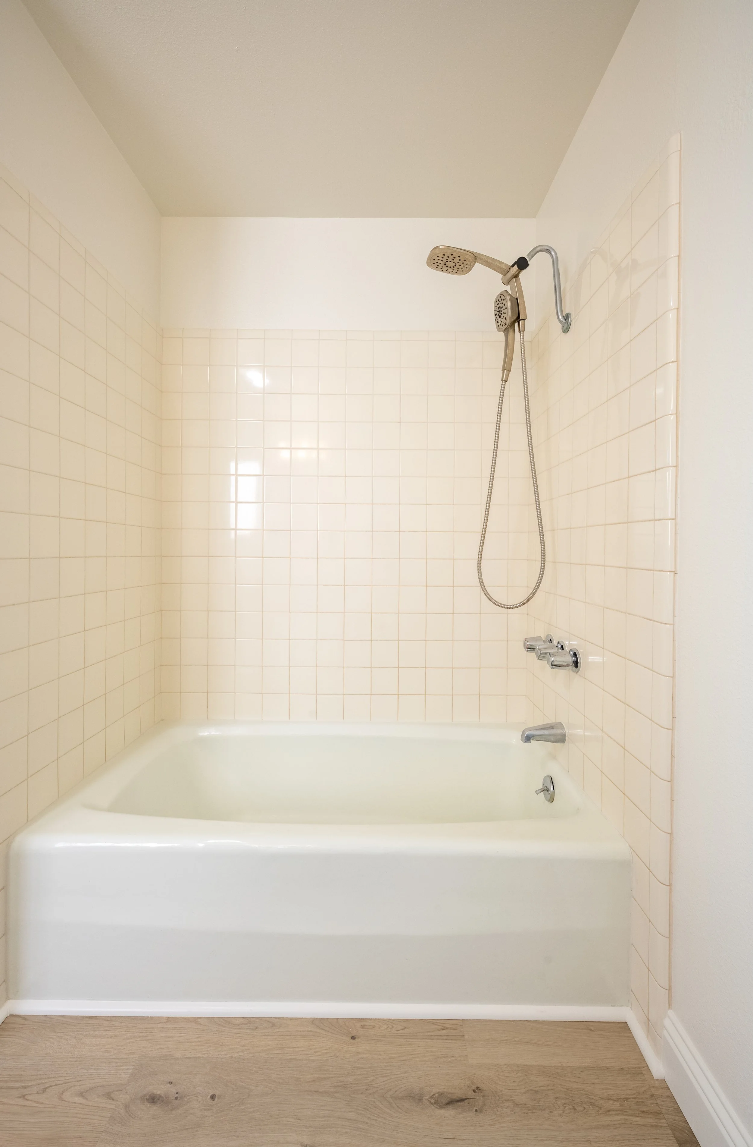 Apt. F Canary Apartments in Calistoga, CA.  A white bathtub with a showerhead and tile wall, situated on a light wooden floor in a bathroom.