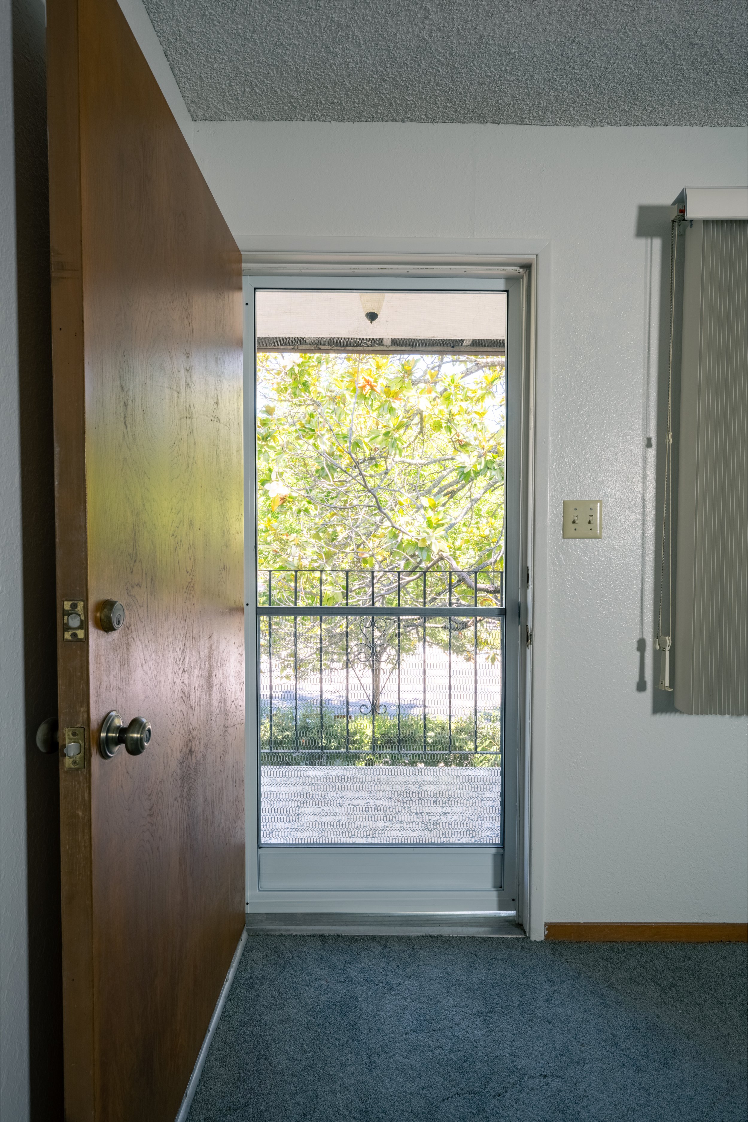 Apt. F Canary Apartments in Calistoga.  Open wooden door leading to a small balcony with a metal railing, overlooking a leafy tree outside.
