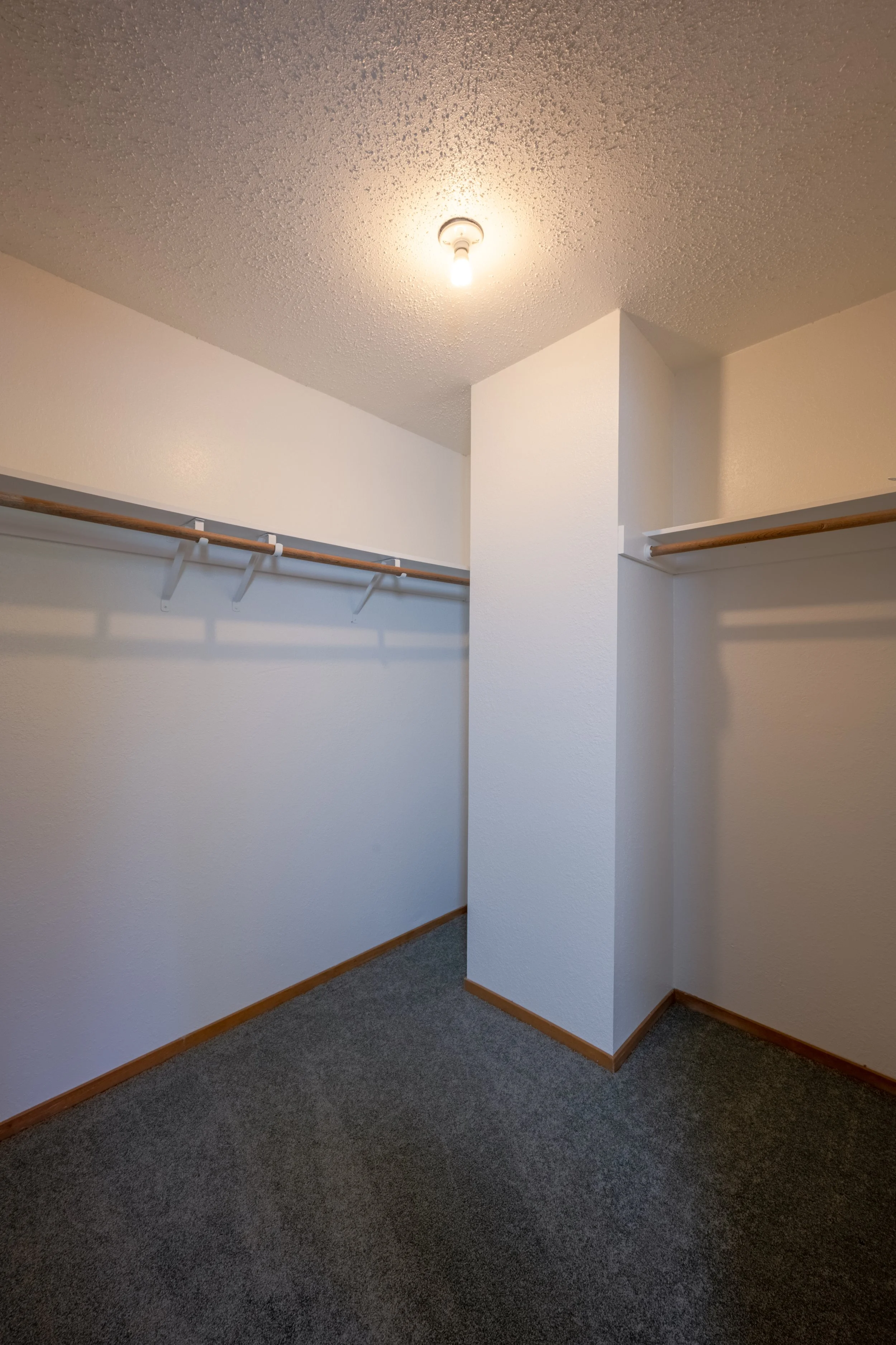 Apt. F Canary Apartments in Calistoga, CA.  Empty walk-in closet with white walls, wooden shelves, and a gray carpeted floor, illuminated by a ceiling light.