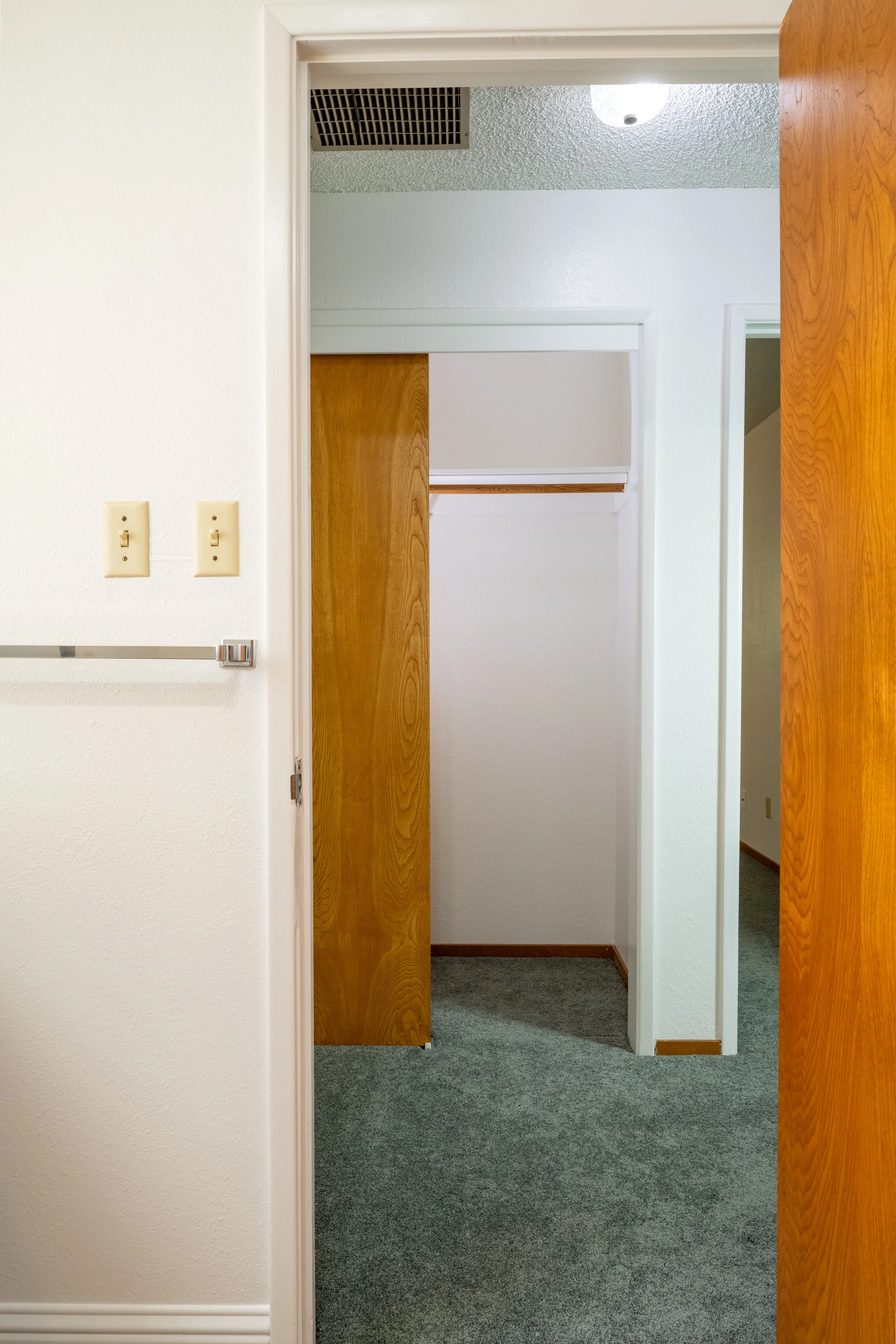 Apt. F: Canary Apartments in Calistoga, CA.   An empty closet with a wooden sliding door, white walls, carpeted floor, and a ceiling vent.