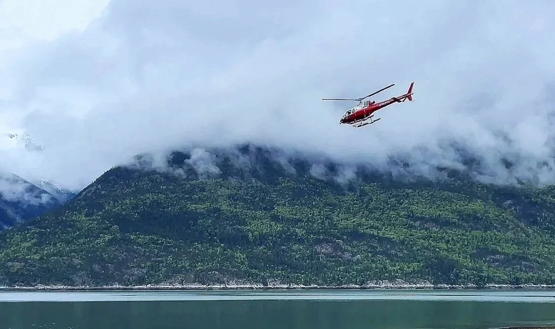 Luxury Travel Marketing. Private Jet Tours Expedition. A helicopter flying over a mountain and lake landscape with cloudy sky.