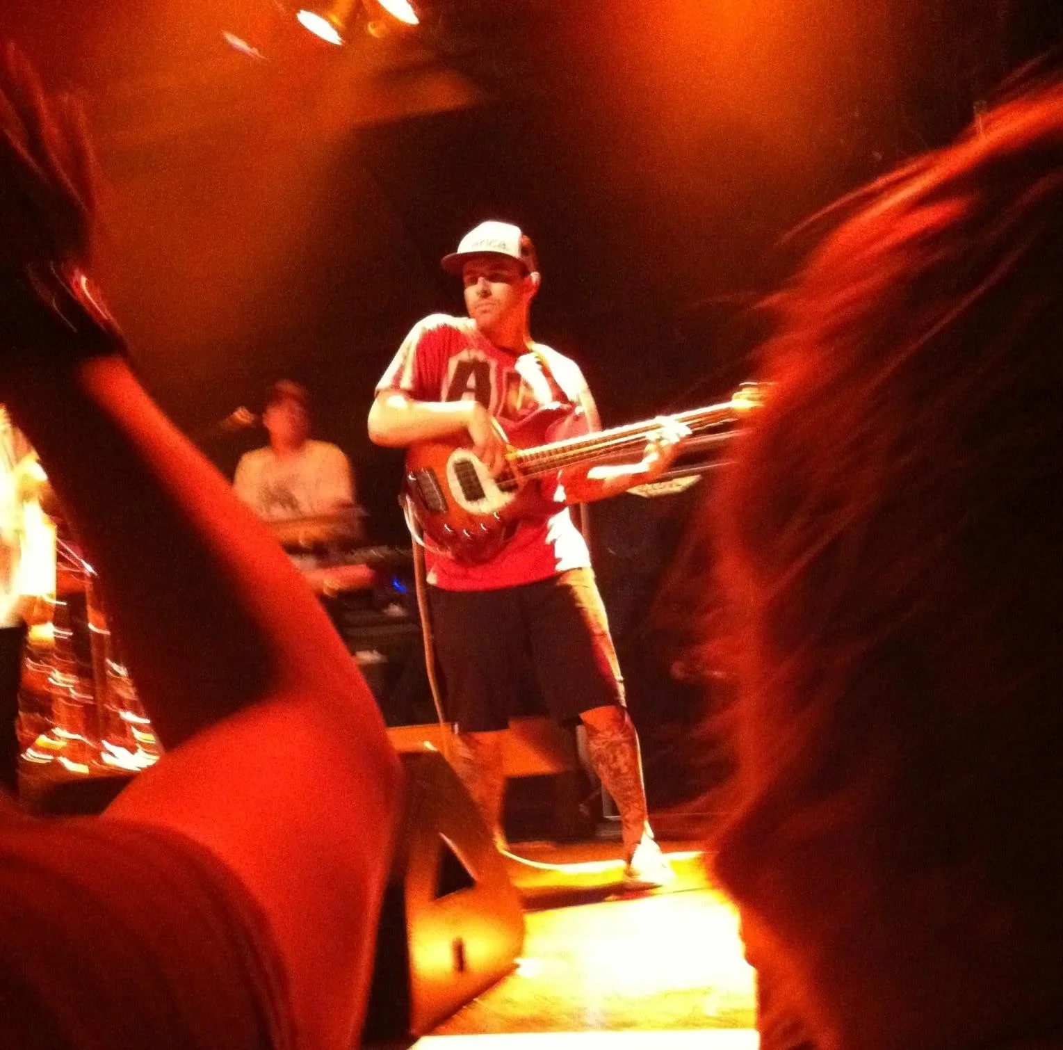 Professional Event Photography. Musician performing on stage with guitar, illuminated by orange stage lights, with audience members visible in the foreground.