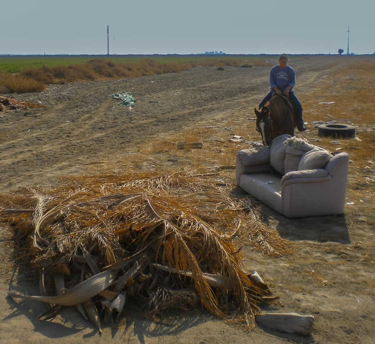Ranae riding a horse past debris and dumped furniture in a field