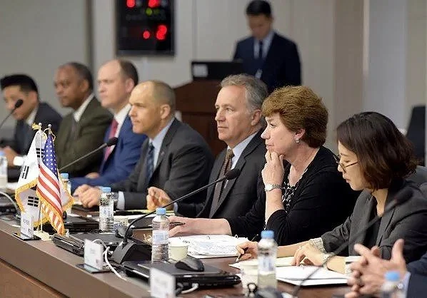 US DOD officials  sitting at a conference table during a formal meeting with ROK Korea, with flags, microphones, and water bottles in front of them.