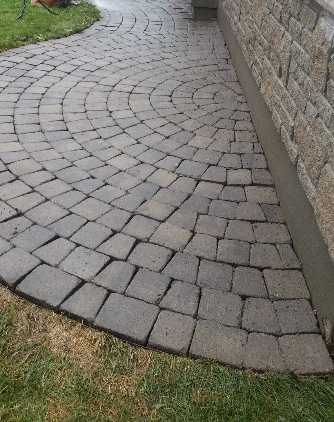 Curved brick walkway beside a brick wall and grass.