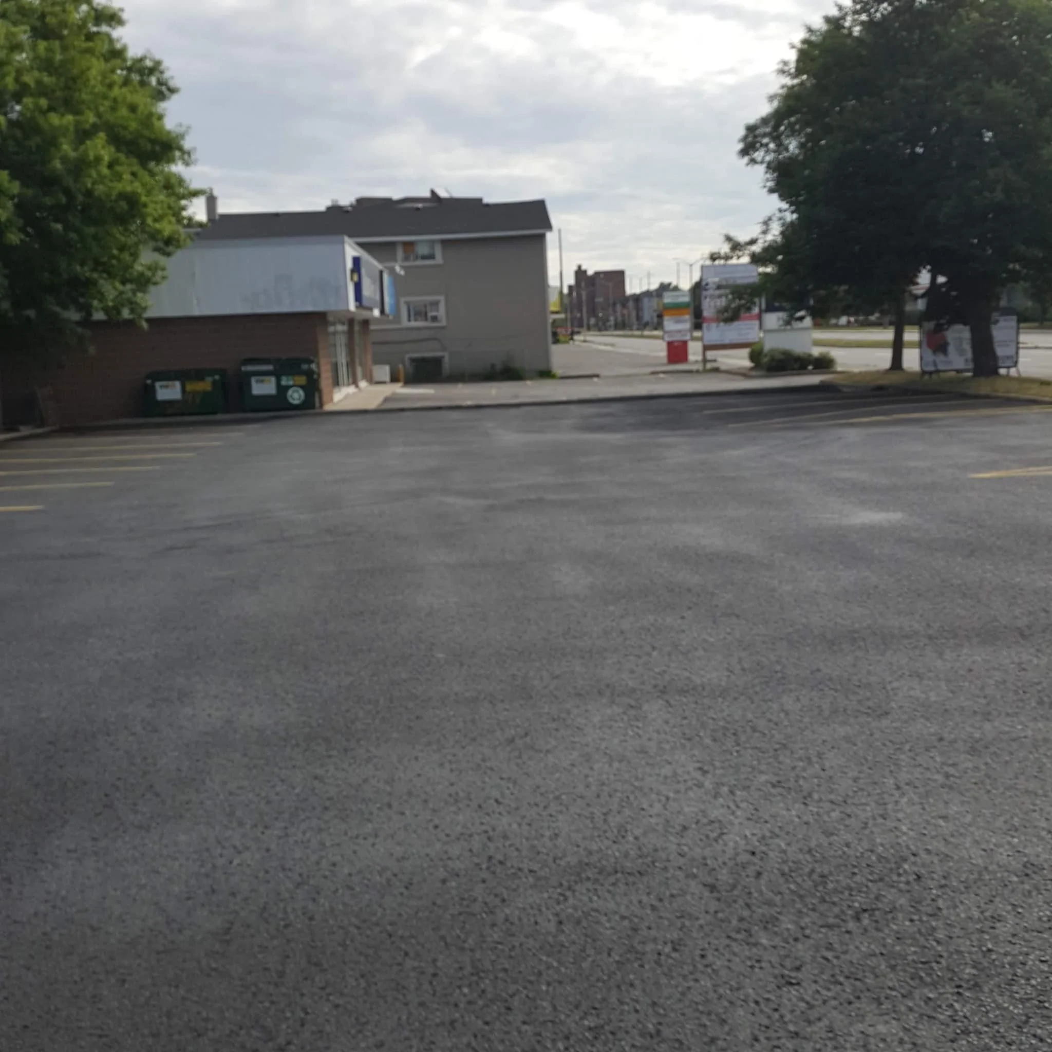 Empty parking lot with a building on the left and trees on the right, in a commercial area on an overcast day.
