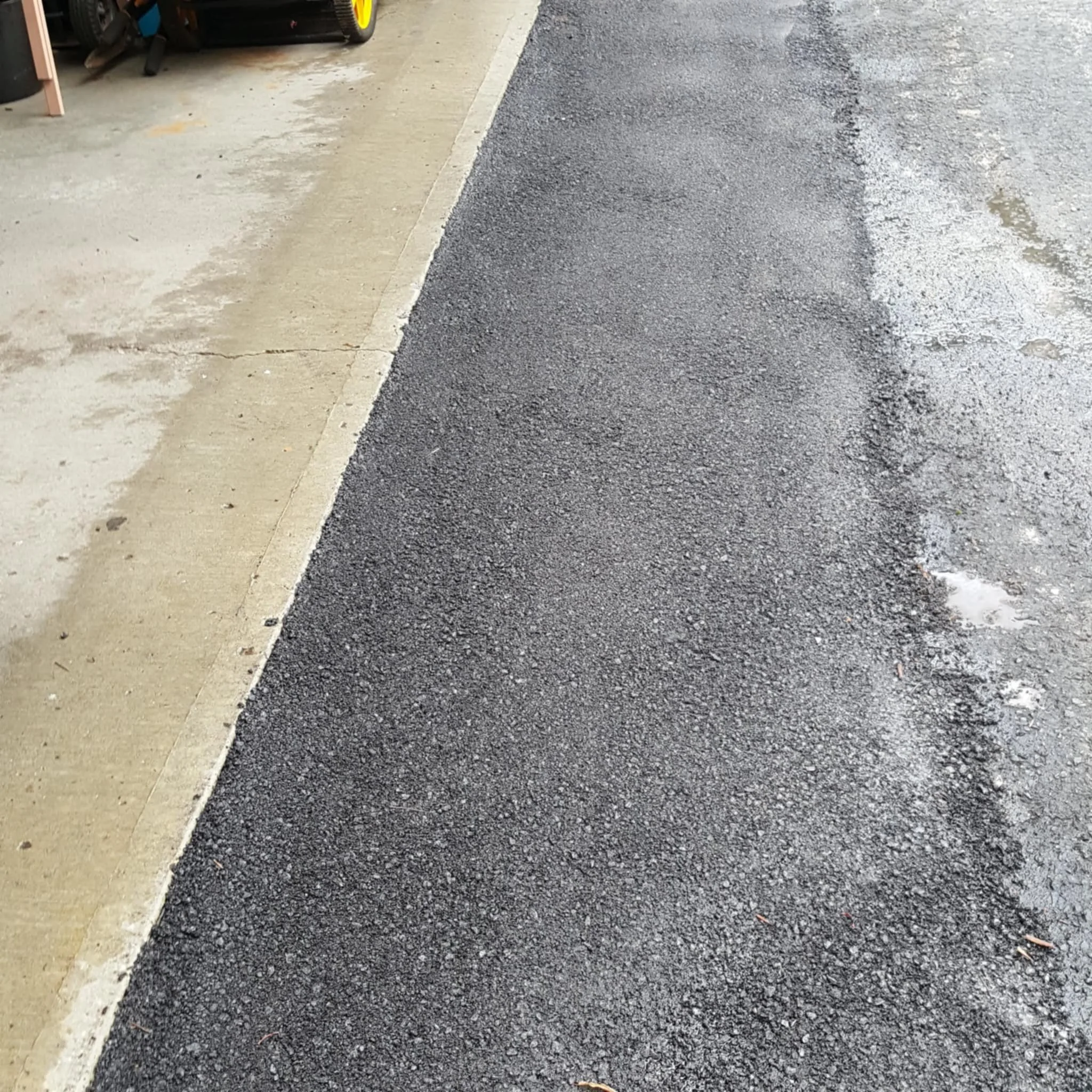 Close-up of a sidewalk and newly paved asphalt roadway, with a curb separating the two surfaces.