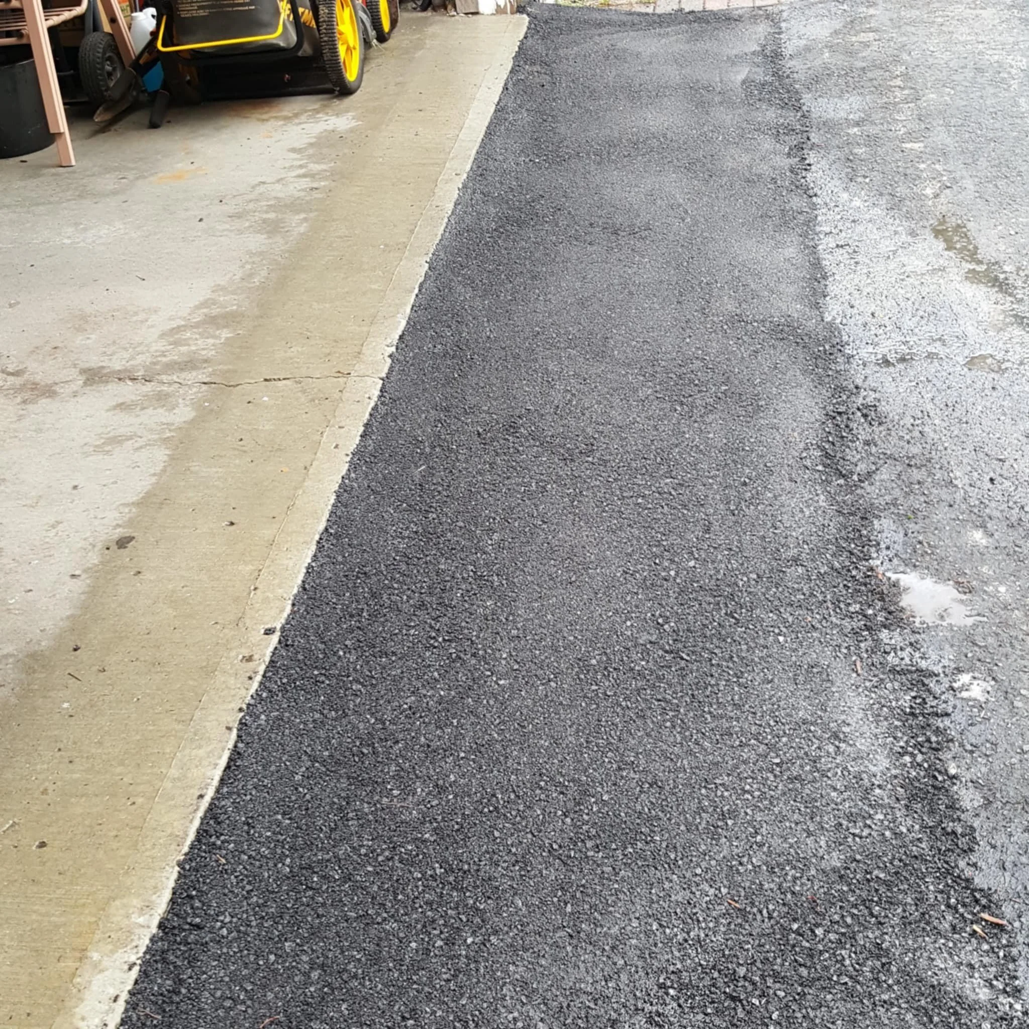 Close-up view of an asphalt sidewalk and a concrete parking lot edge with some patches of white snow or ice.