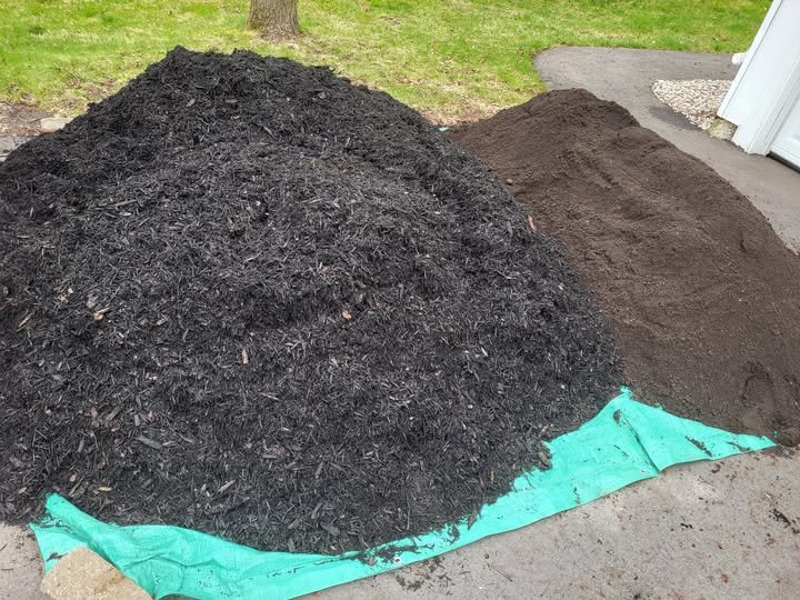 Two piles of soil or mulch, one dark and the other brown, on a patio next to a light blue tarp with grass and a tree in background.