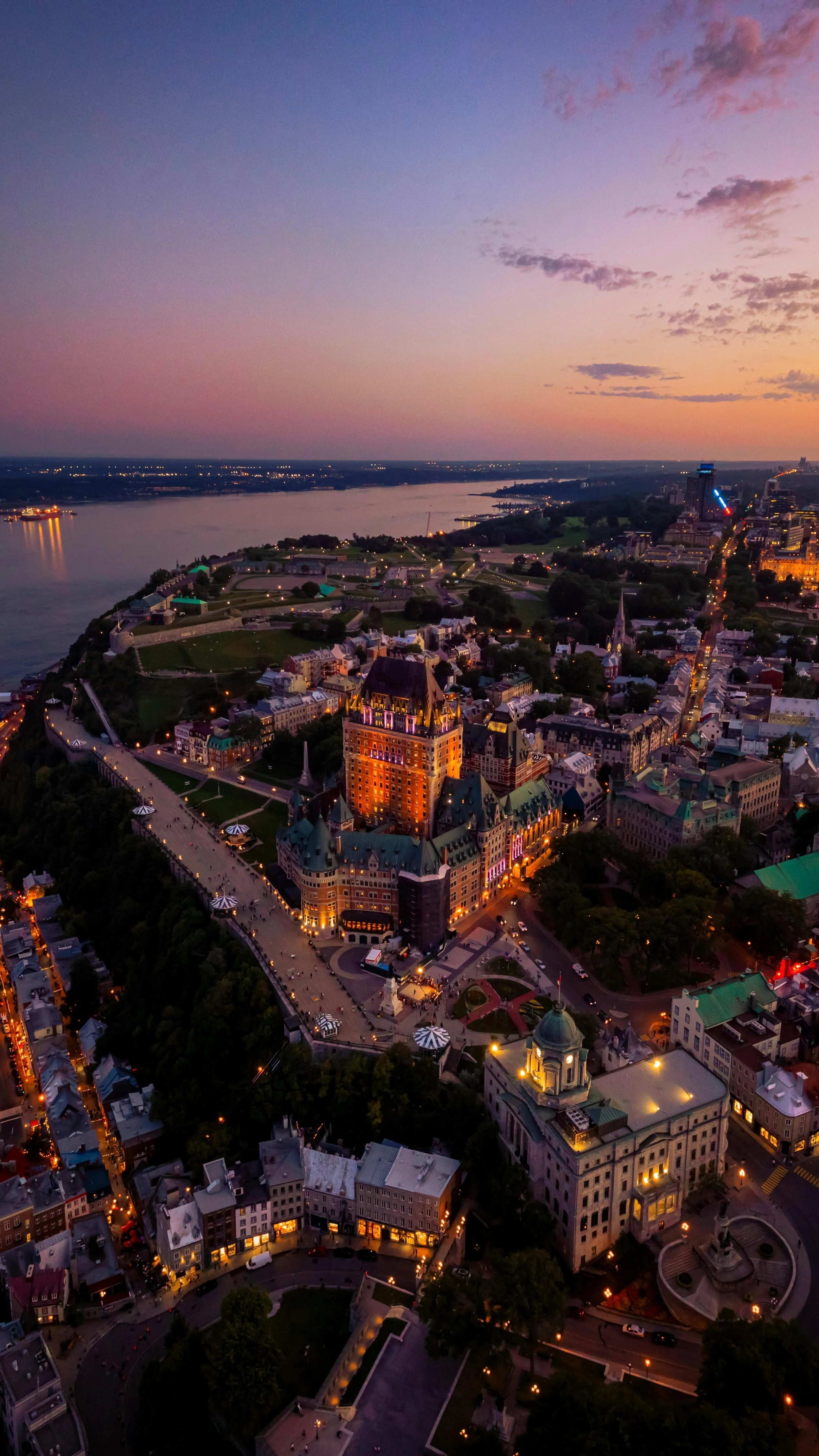 Vue aérienne de la ville de Québec au coucher du soleil, mettant en valeur le Château Frontenac, la rivière Saint-Charles et la vieille ville illuminée.