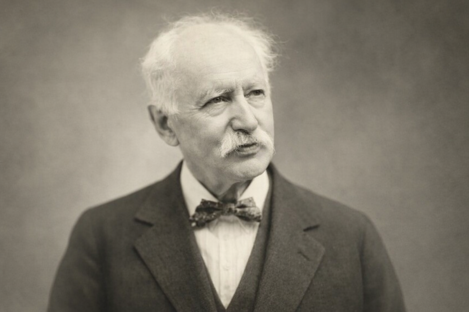 Portrait en noir et blanc d'un homme âgé avec une moustache, portant un costume avec un nœud papillon, regardant vers la droite.