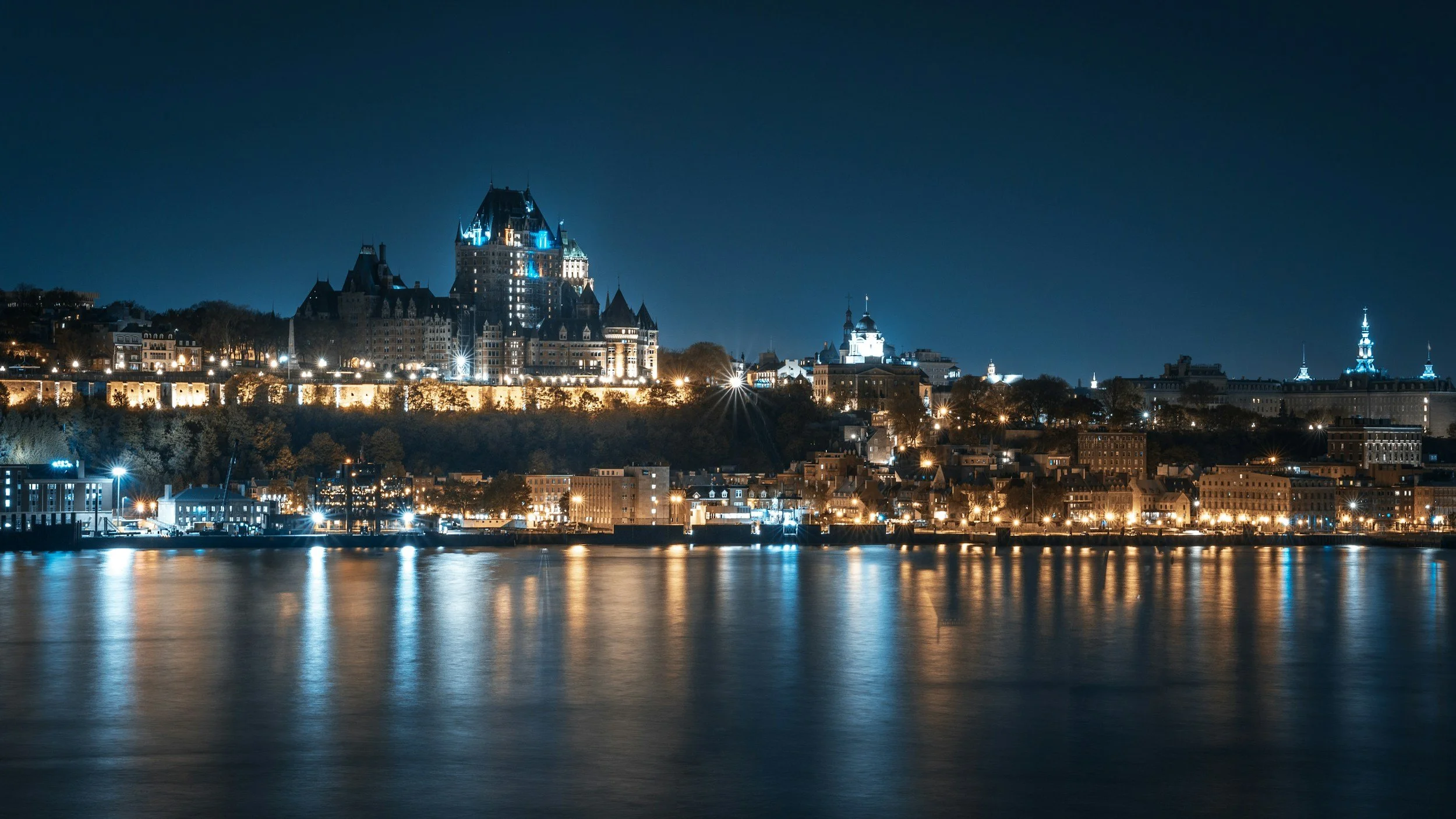 Vue nocturne du Château Frontenac et du fleuve Saint-Laurent à Québec, illuminés avec reflet dans l'eau.