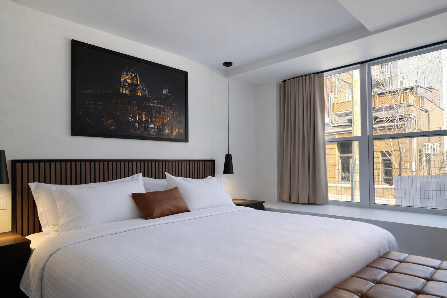 Chambre d'hôtel avec lit blanc, tableau de nuit, côté fenêtre avec vue sur bâtiments et arbres, rideaux beiges.