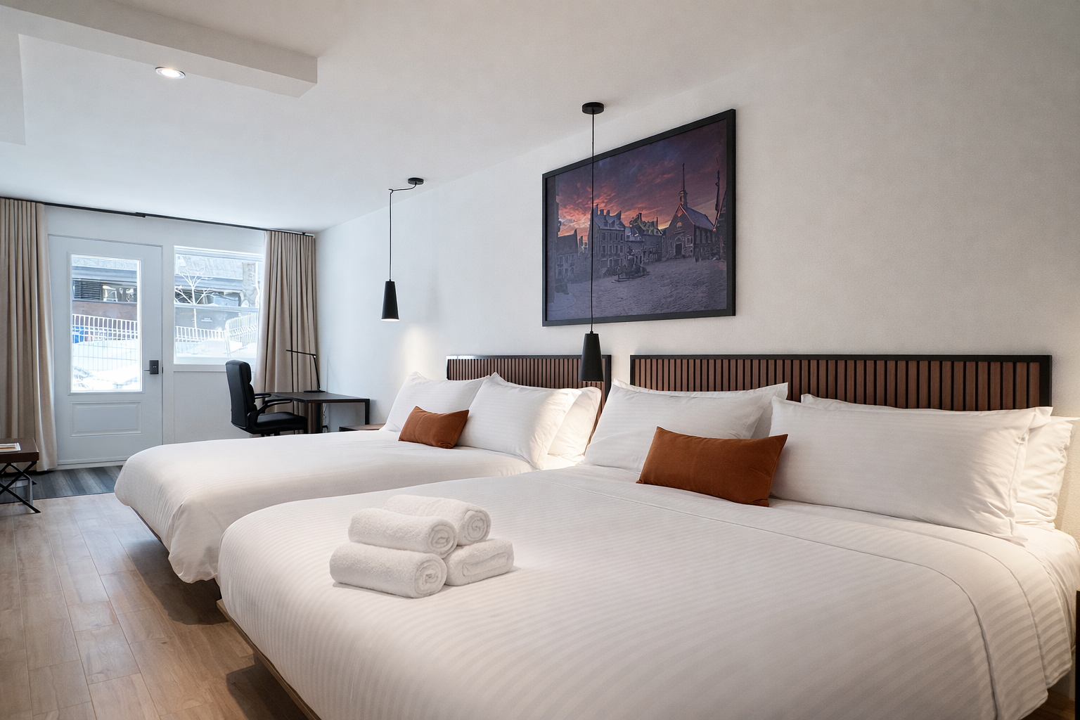 Chambre d'hôtel avec deux lits doubles, rouleaux de serviettes, tableau sur le mur, bureau avec chaise, vue sur la neige extérieure, rideaux beige.