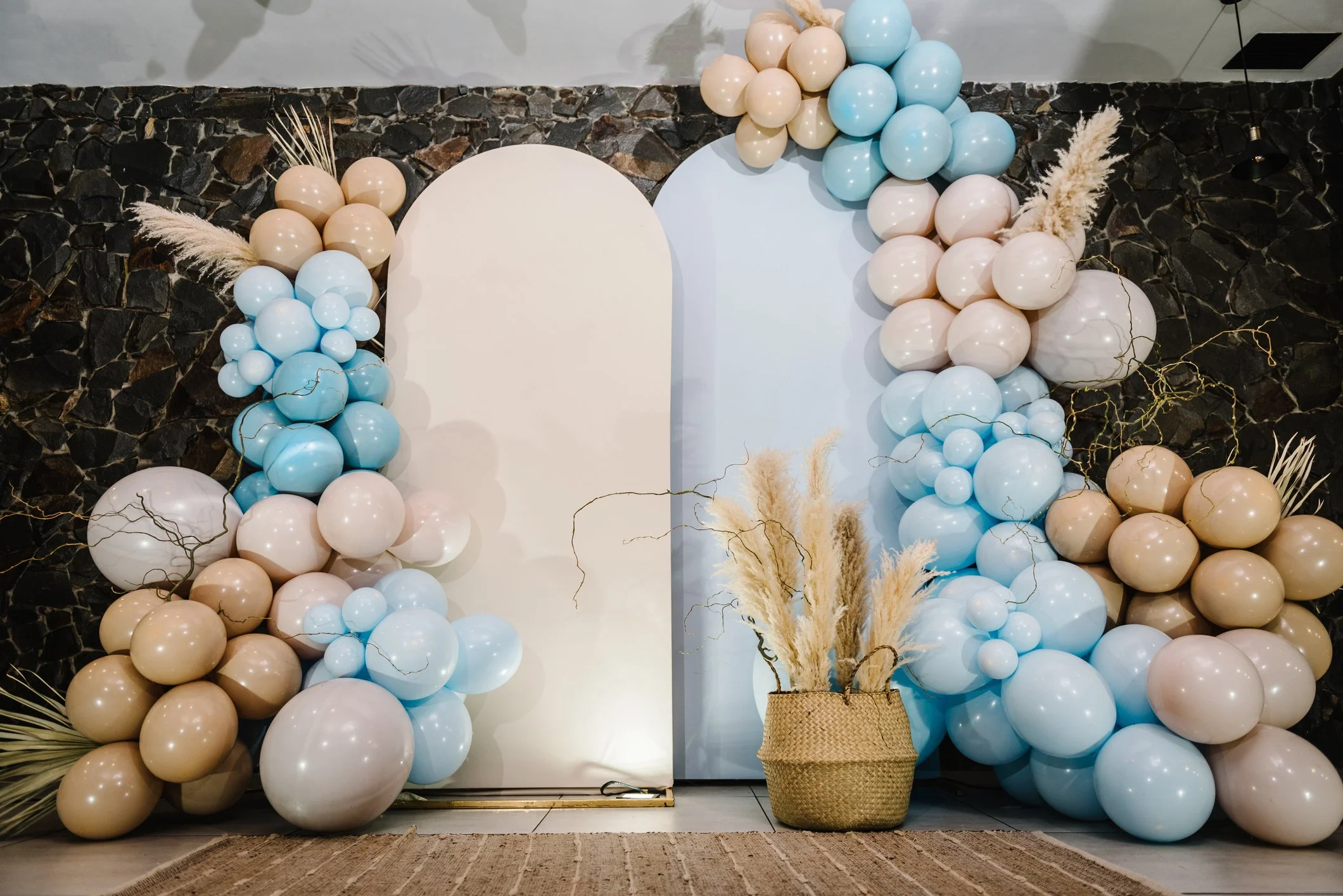 Decorative balloon arrangement in pastel colors with pampas grass in a basket, set against white and light blue panels.
