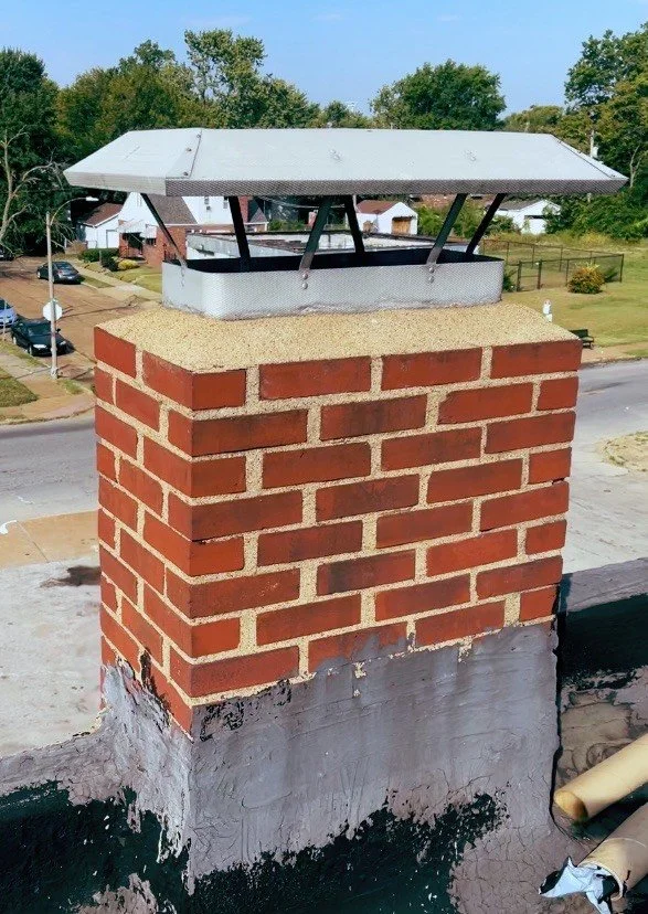 A modern wooden house with large glass windows, a concrete and stone staircase leading up to a patio, set in a hilly landscape with mountains in the background.