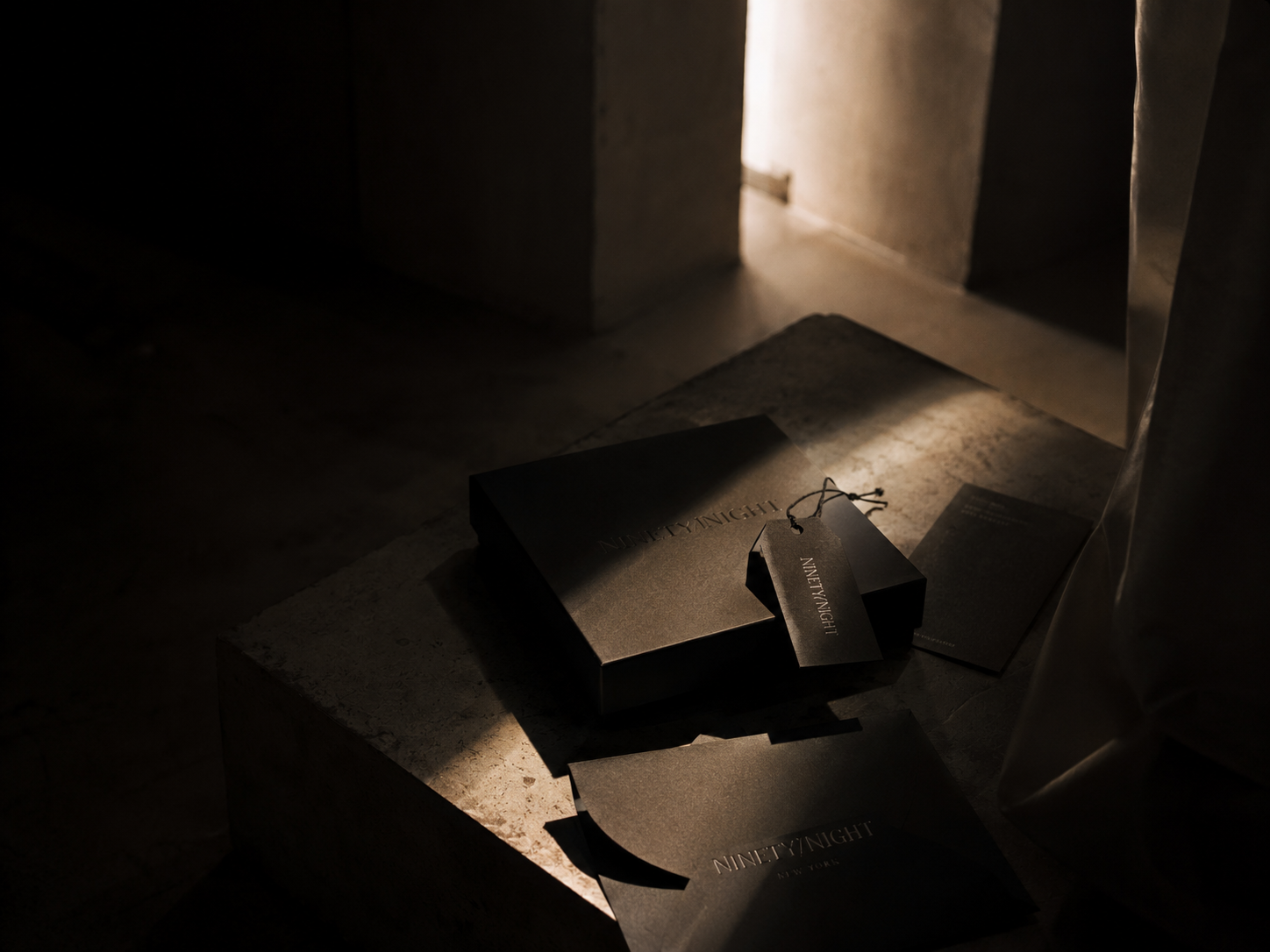 Darkly lit scene with black shopping bags and a booklet on a stone surface, illuminated by a beam of light coming from a nearby doorway.