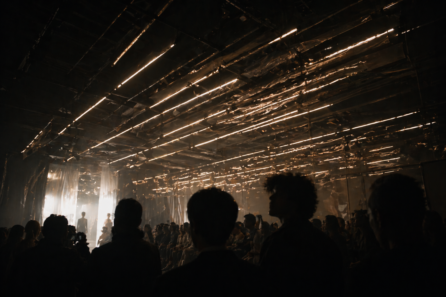 Silhouettes of people attending a fashion show or event, with a dark room and shiny, metallic ceiling reflecting light.