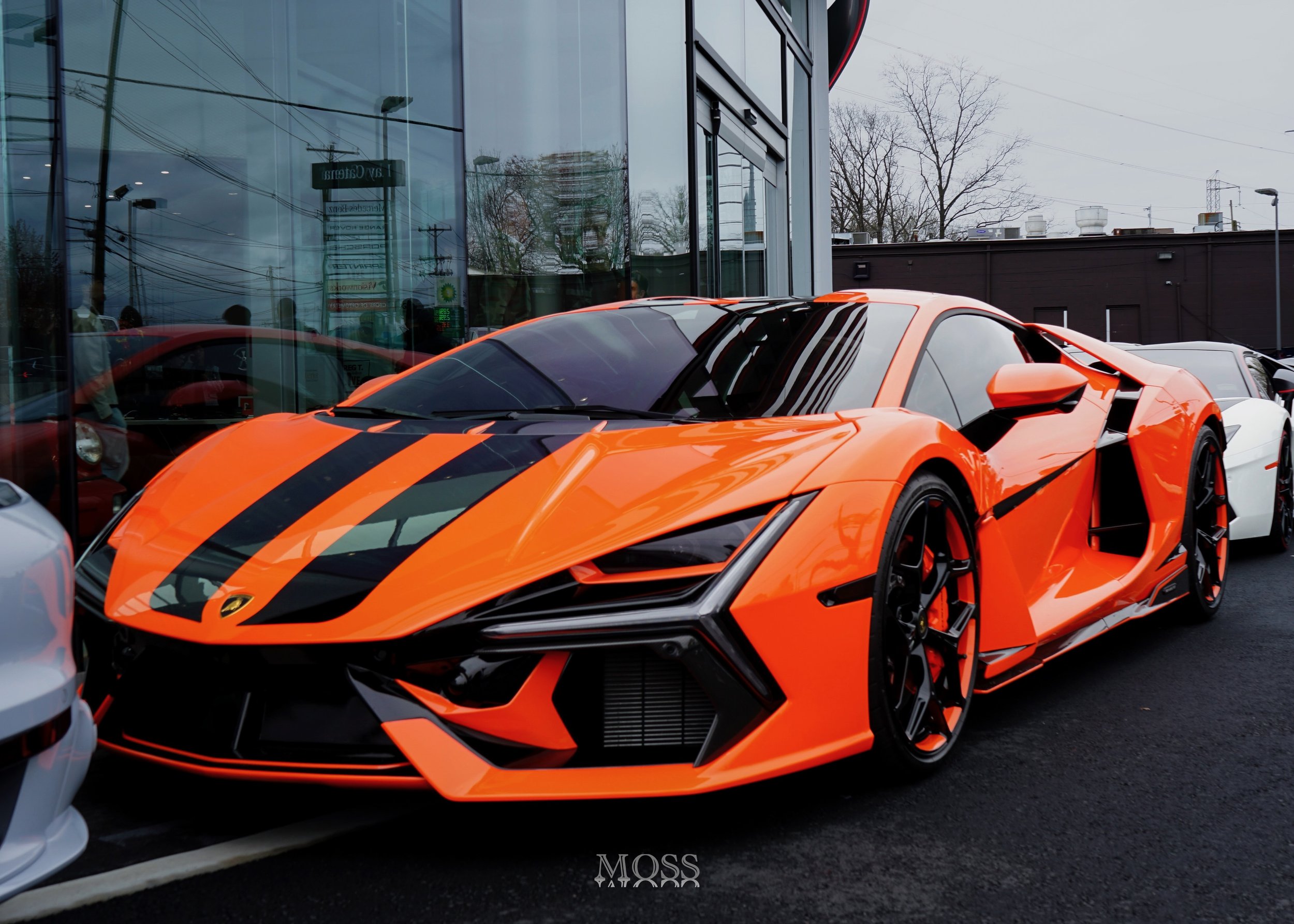 An orange and black Lamborghini sports car parked outside a building with glass windows.