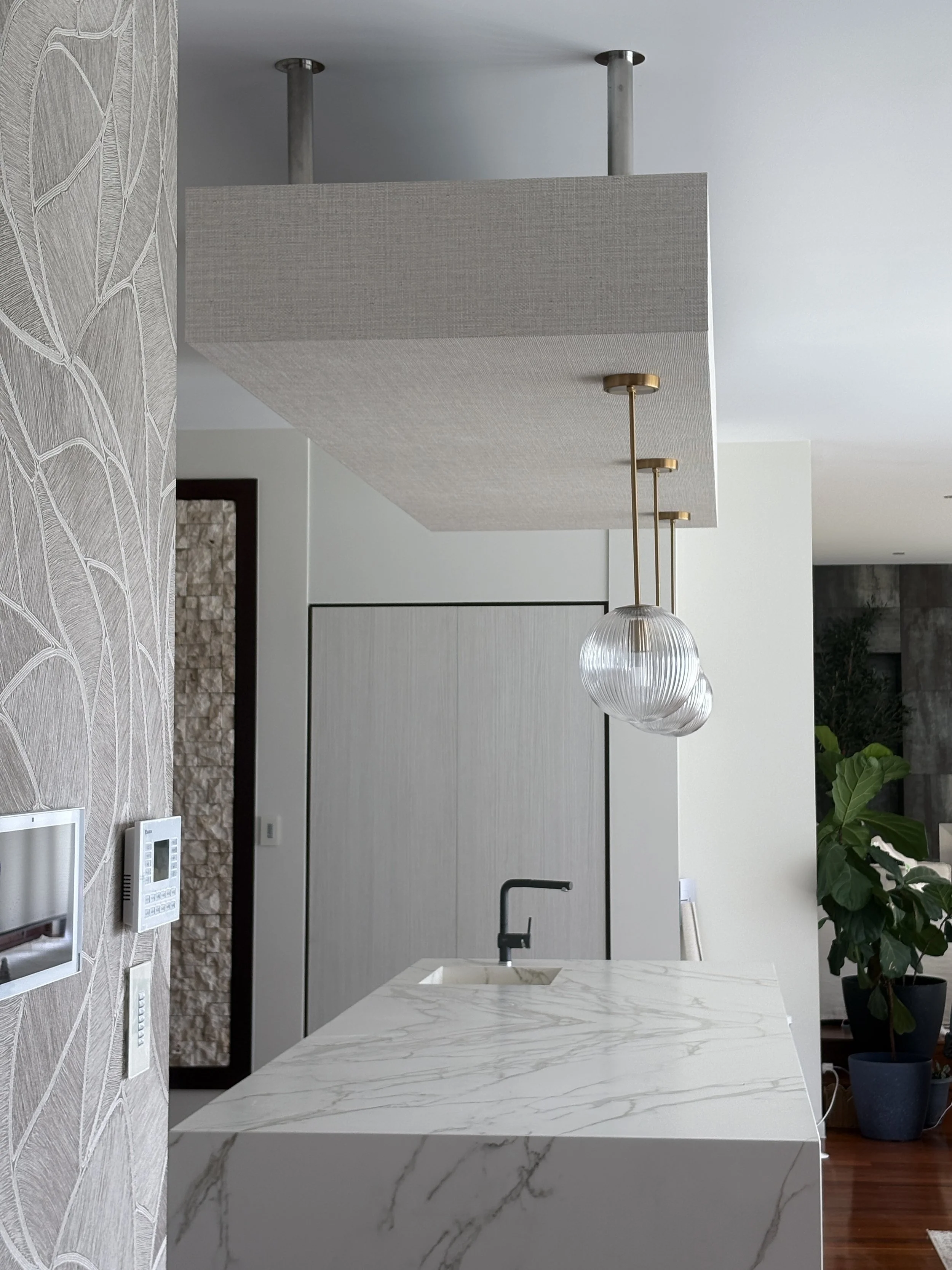 A person standing on a ladder in a room with white walls, installing or inspecting a ceiling with ornate, framed fresco artwork depicting a classical or mythological scene.