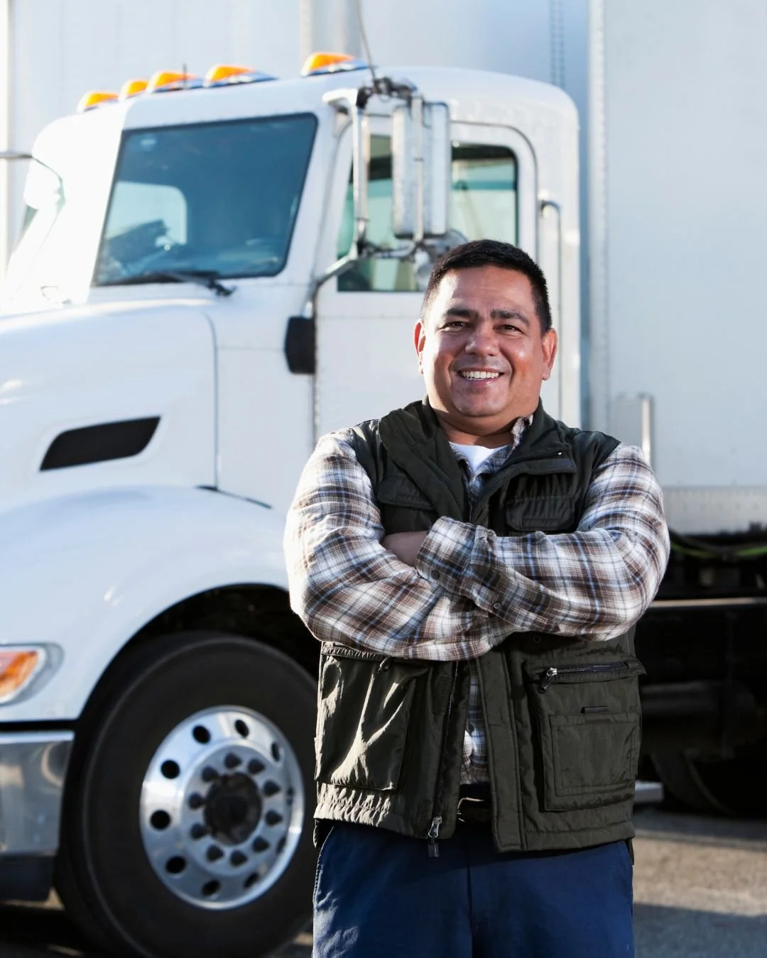 A smiling man with arms crossed standing in front of a large white semi-truck.