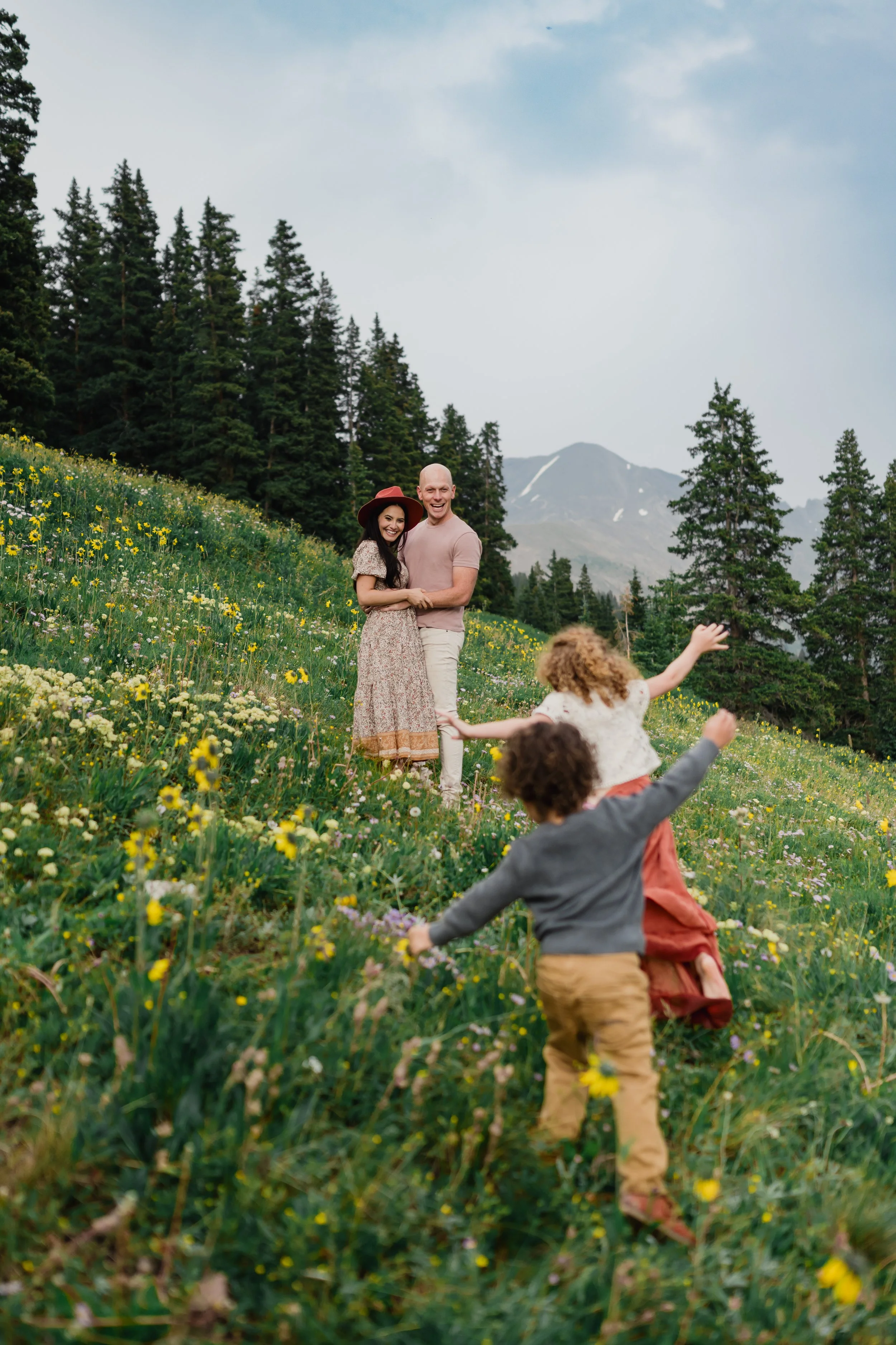 Playful family moment in a vibrant mountain meadow, with children running toward their smiling parents.