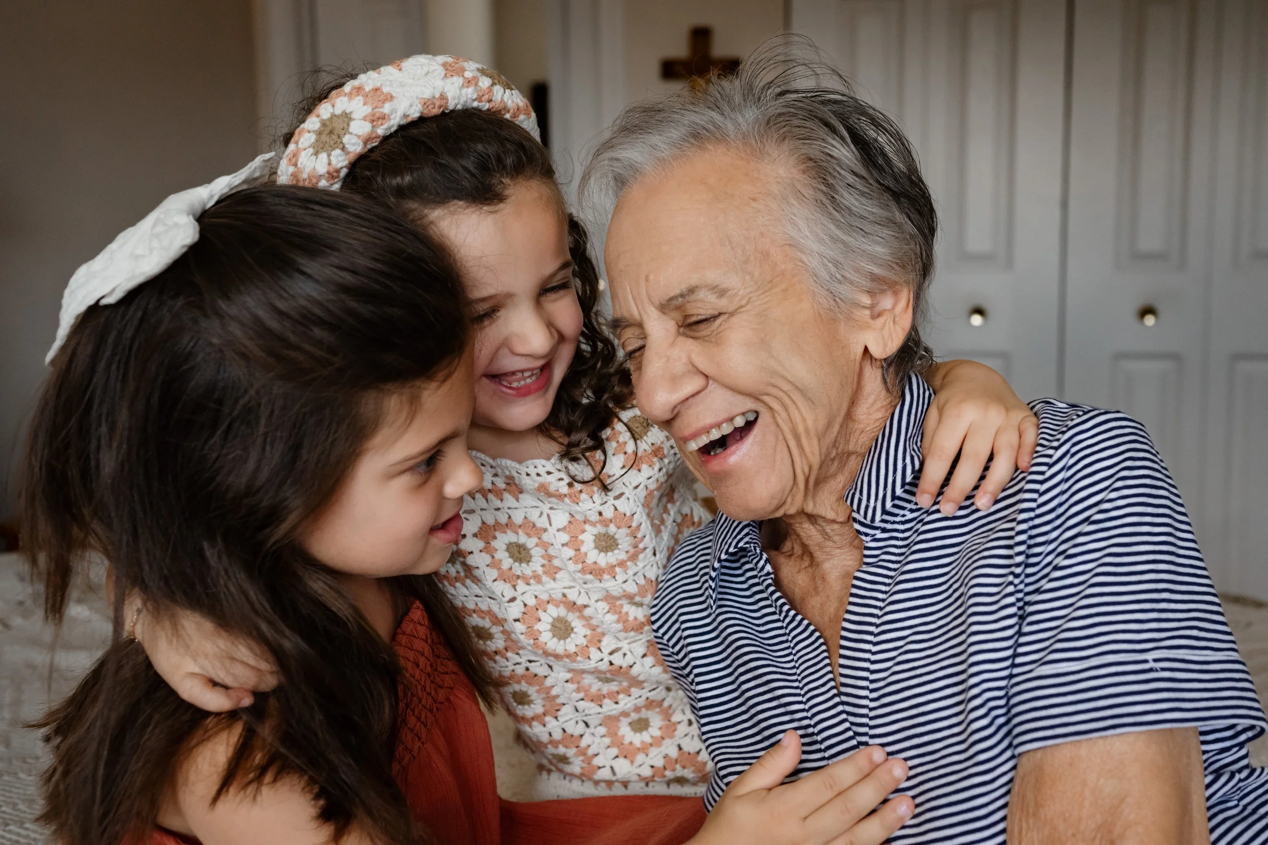A candid and emotional lifestyle portrait of a grandmother joyfully embracing her two granddaughters.