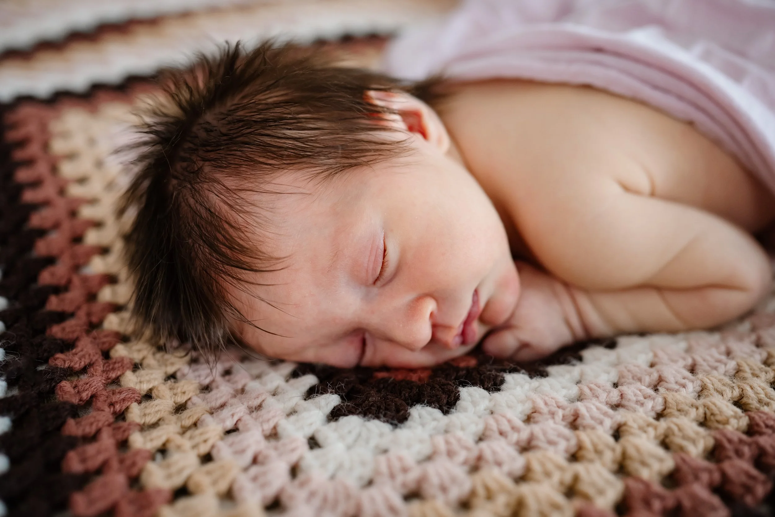Newborn baby peacefully sleeping on their side on a textured knit blanket, with soft natural light highlighting delicate features.