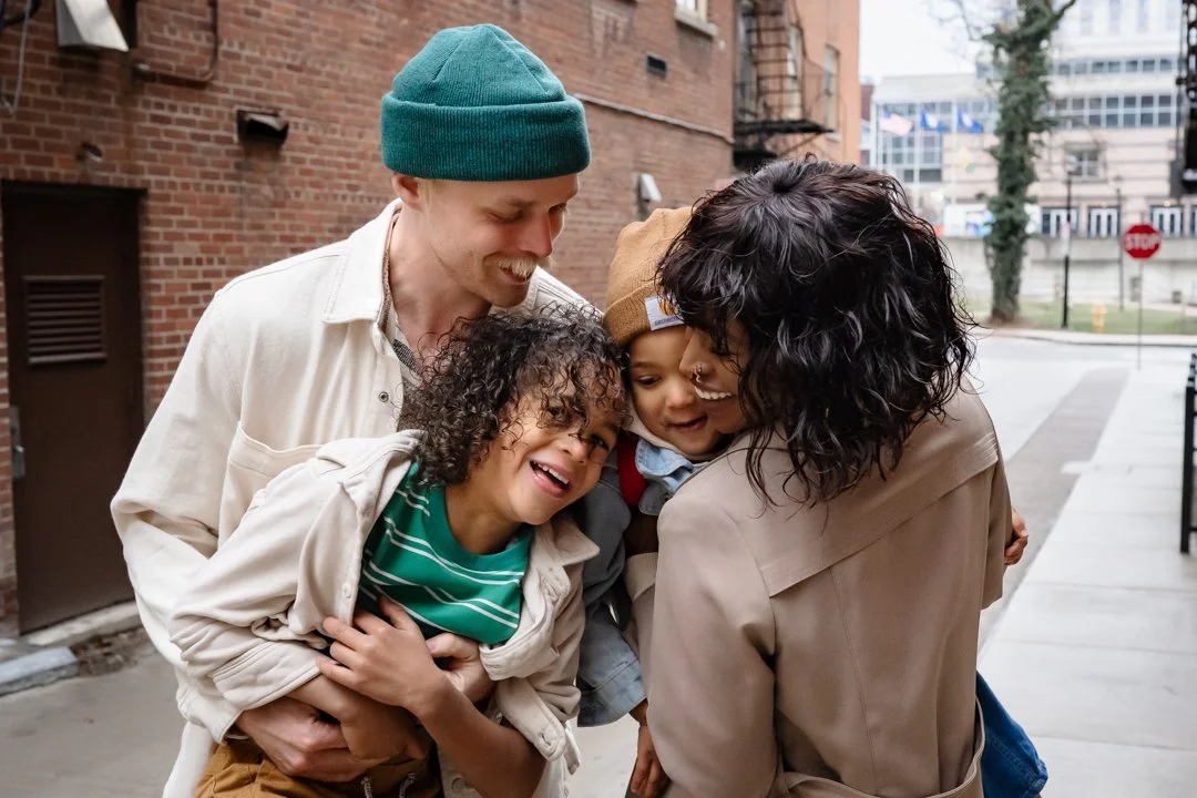 Candid moment of a joyful, stylish family laughing and embracing in an urban alleyway.