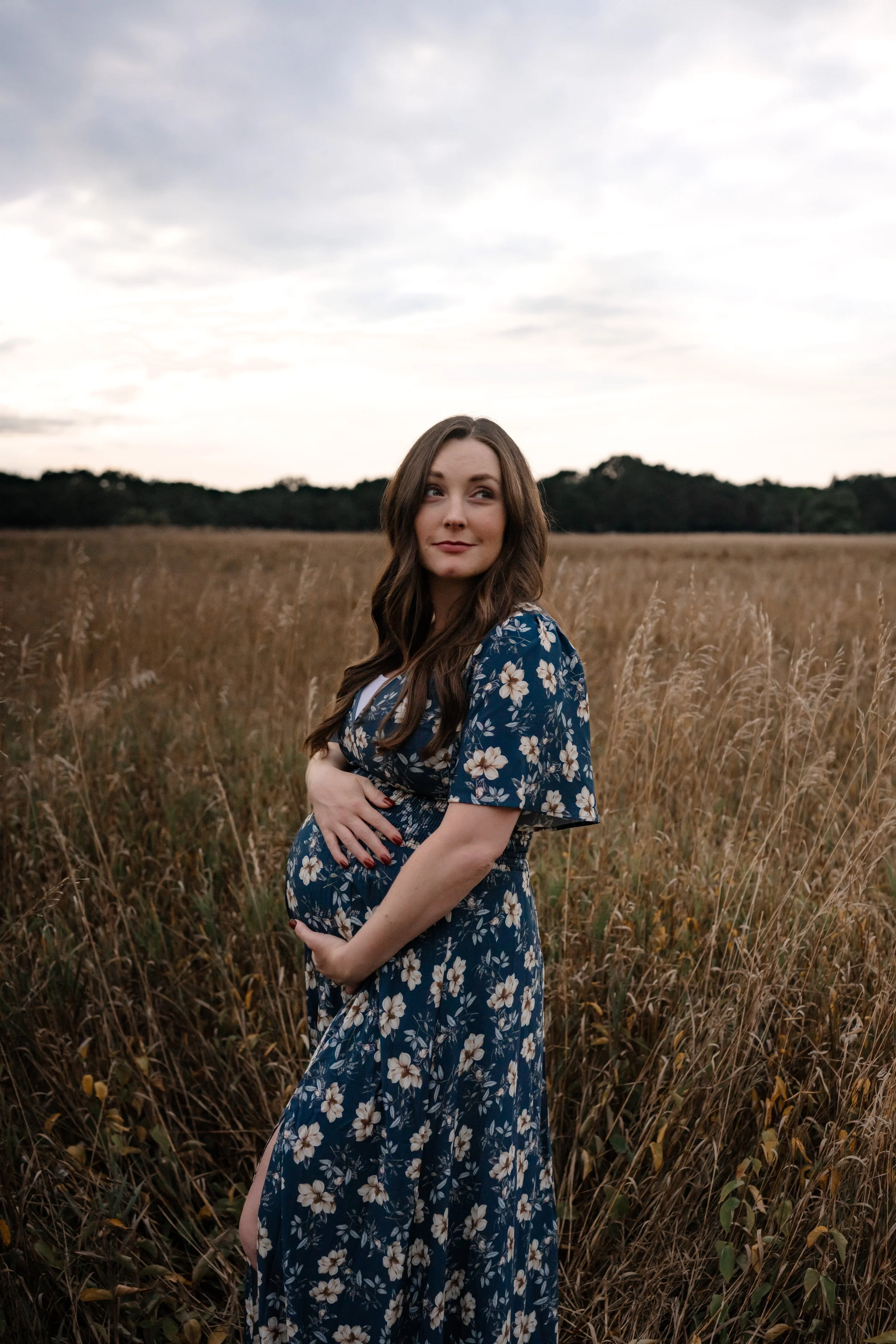Expectant mother cradling her baby bump in a field during an outdoor maternity photography session in Rochester, NY.