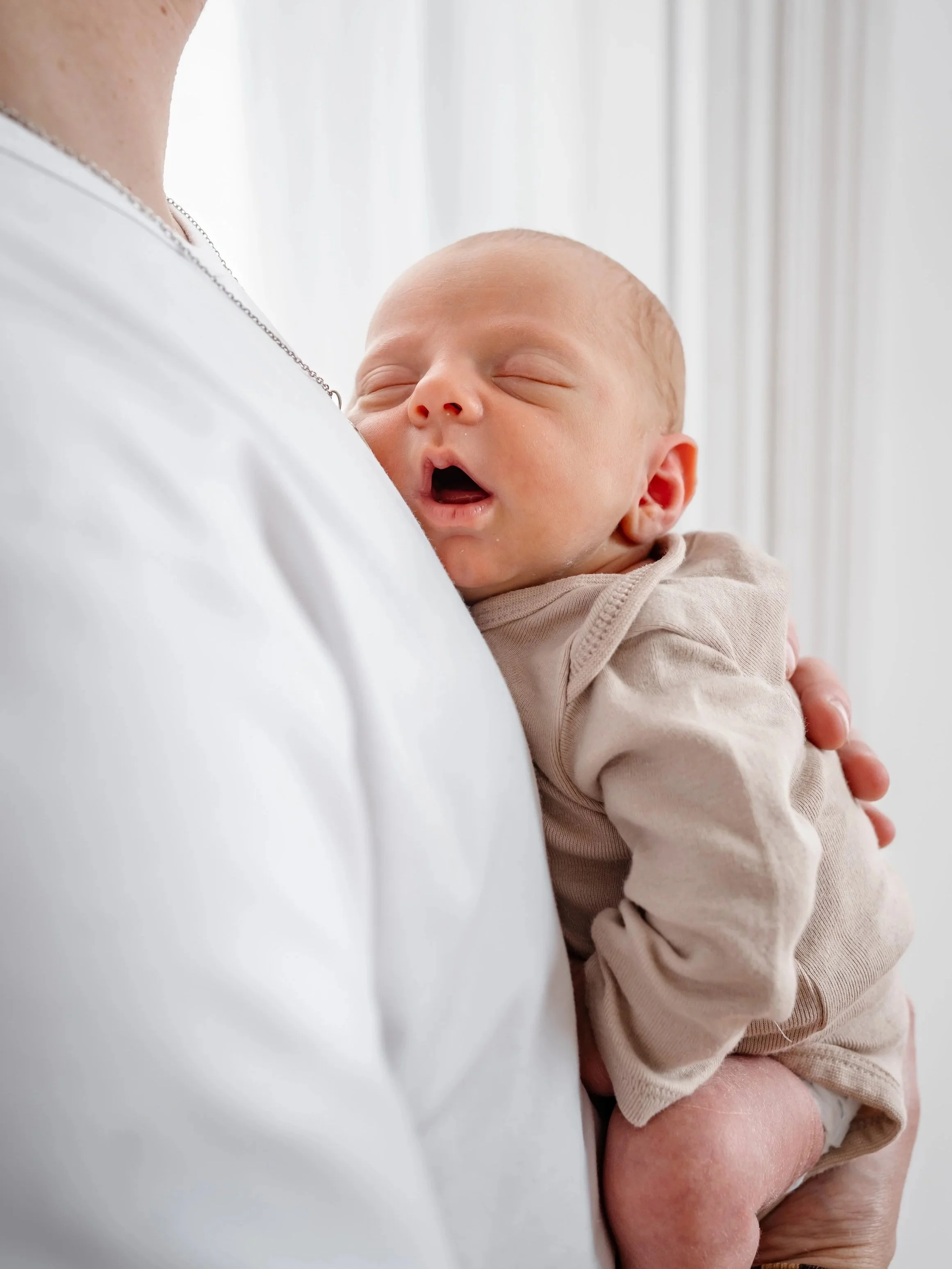 A person holding a sleeping baby against their chest. The baby has a peaceful, sleeping expression with eyes closed and mouth slightly open.
